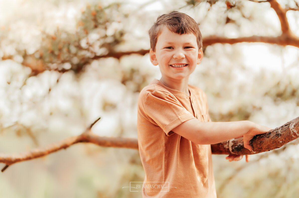 Foto van een jongen die een boomtak vasthoudt en lachend naar de camera kijkt bij de Drunense Duinen