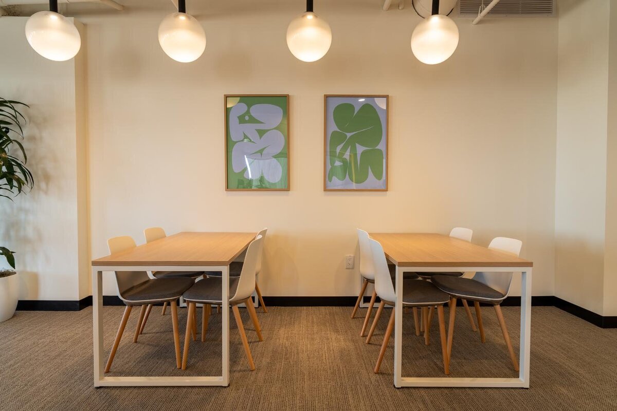 Small dining area featuring two wood tables, white chairs, and abstract green artwork on the wall.