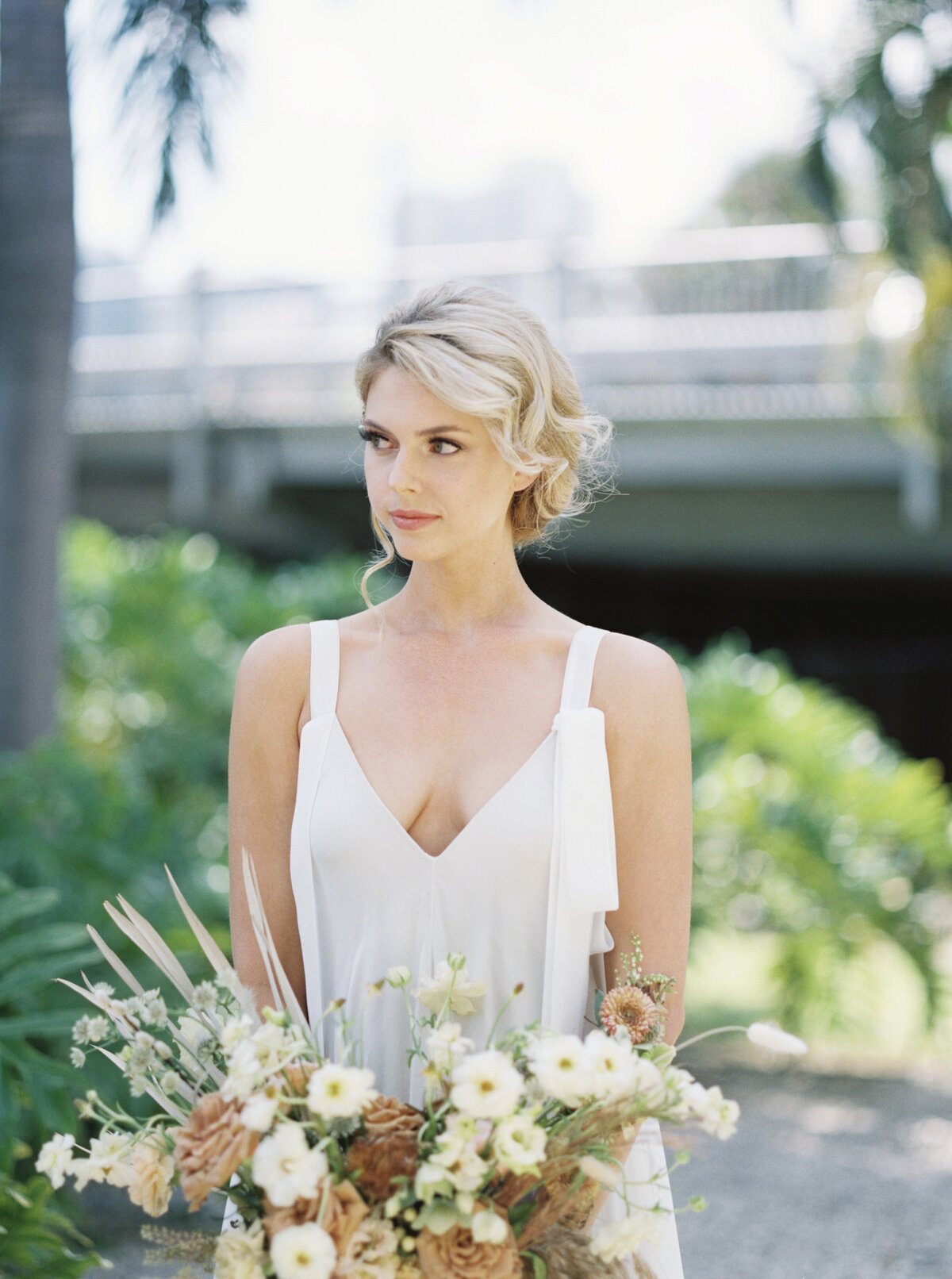 A bride stands ready with her bouquet. She's blonde.