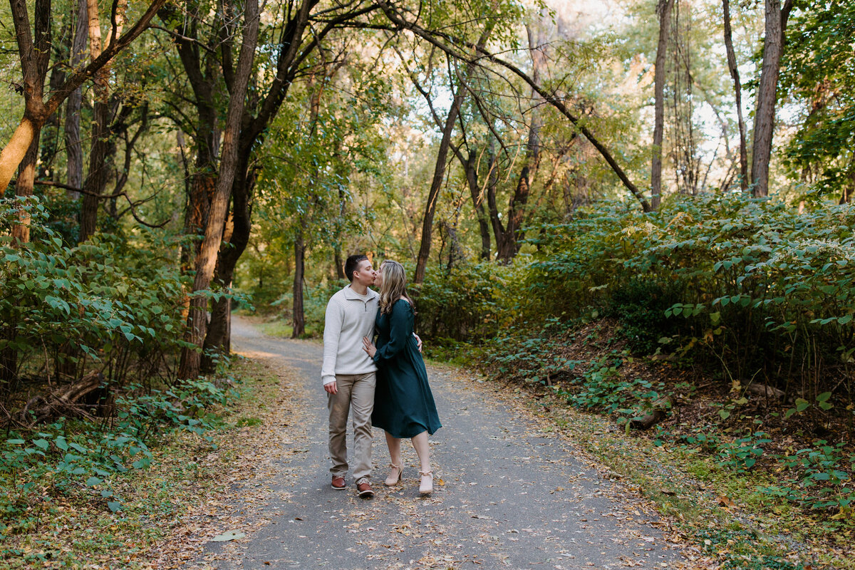 couple with their arms around each other kissing as they walk along a path