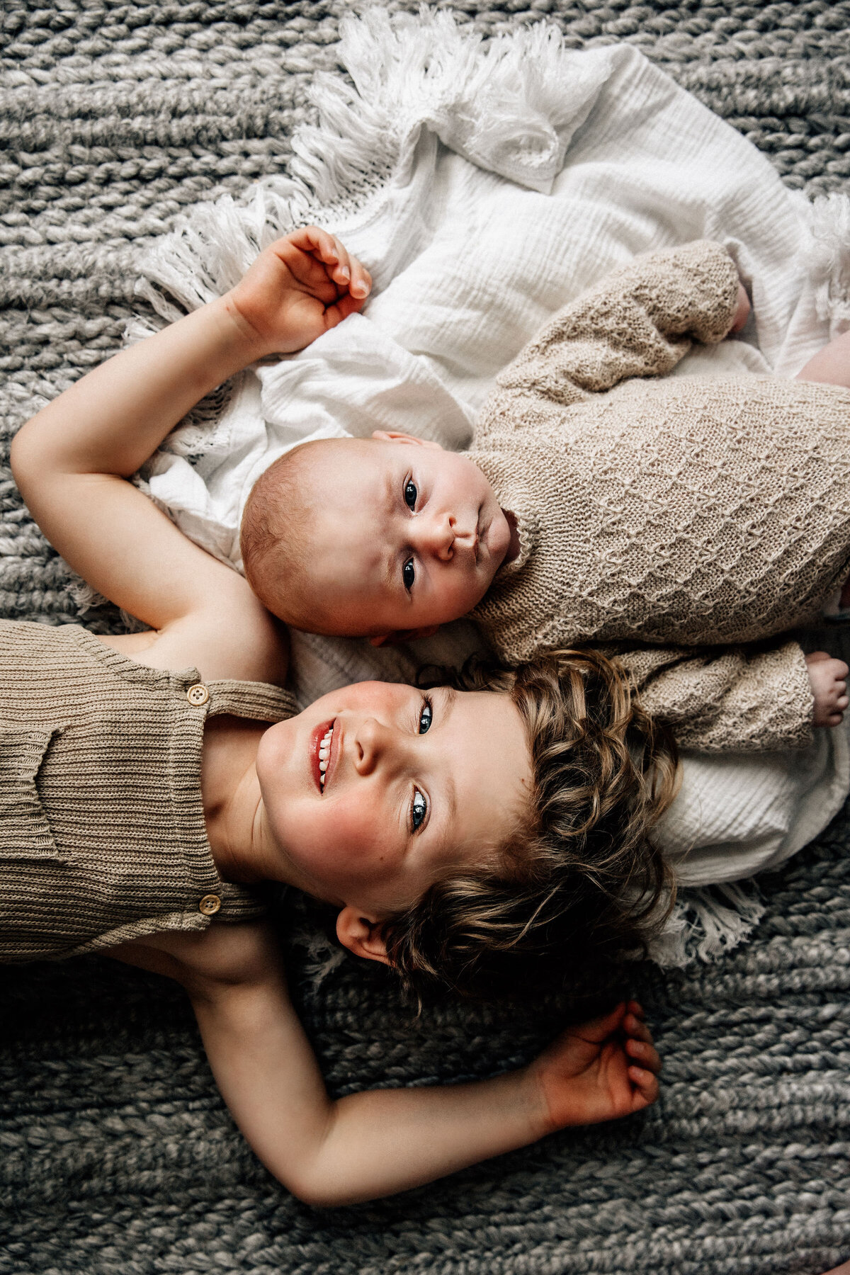 Newborn and toddle rbrother lay looking up at camera