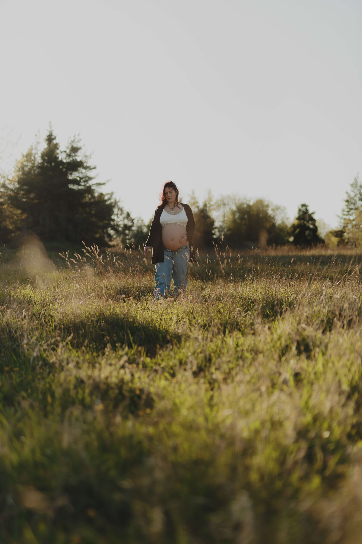 En gravid kvinna gåendes genom gräset under solnedgången under en hudnära gravidfotografering i Stockholm