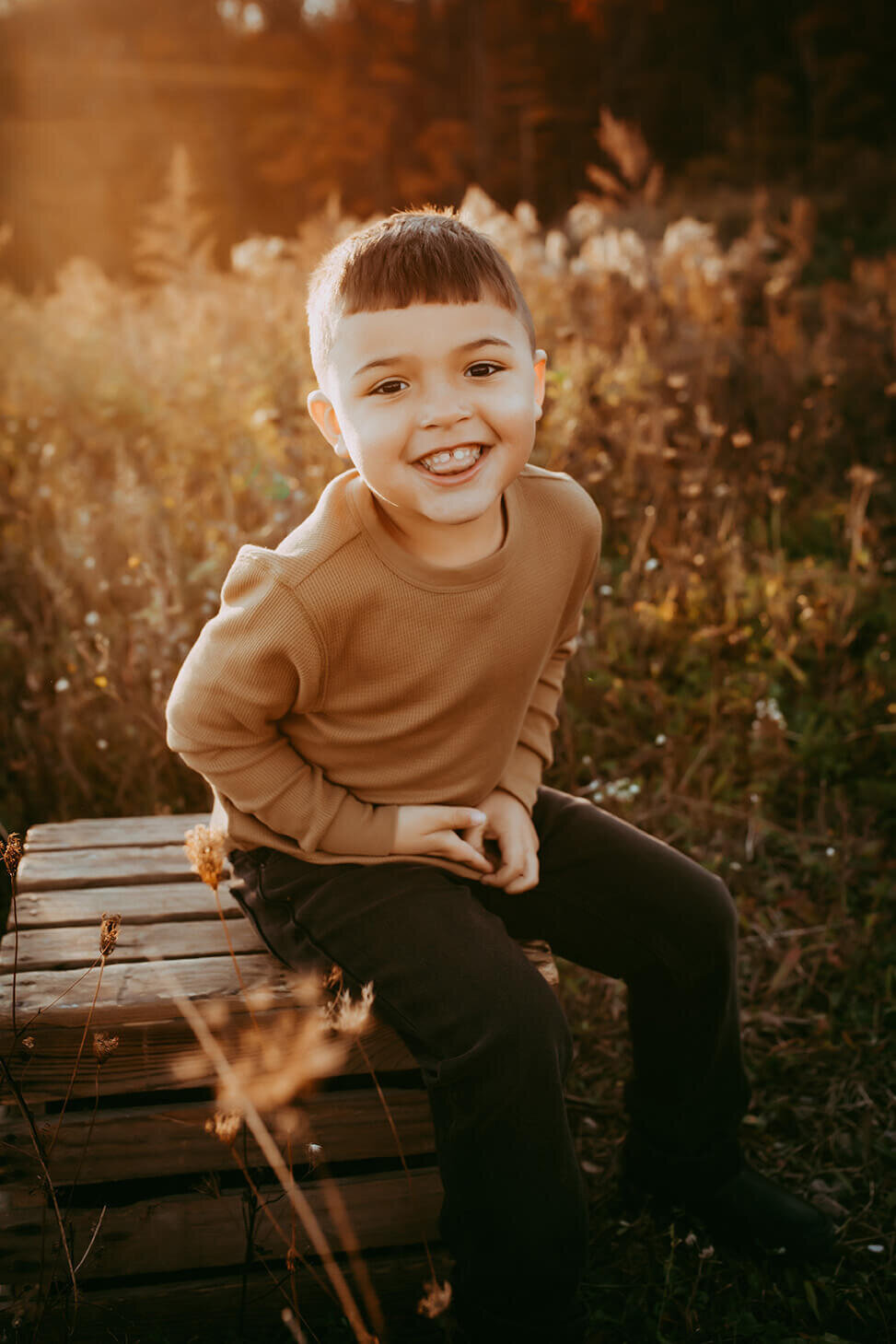a five year old boy sitting on a wooden crate in a field in rochester, ny sticking his tongue out