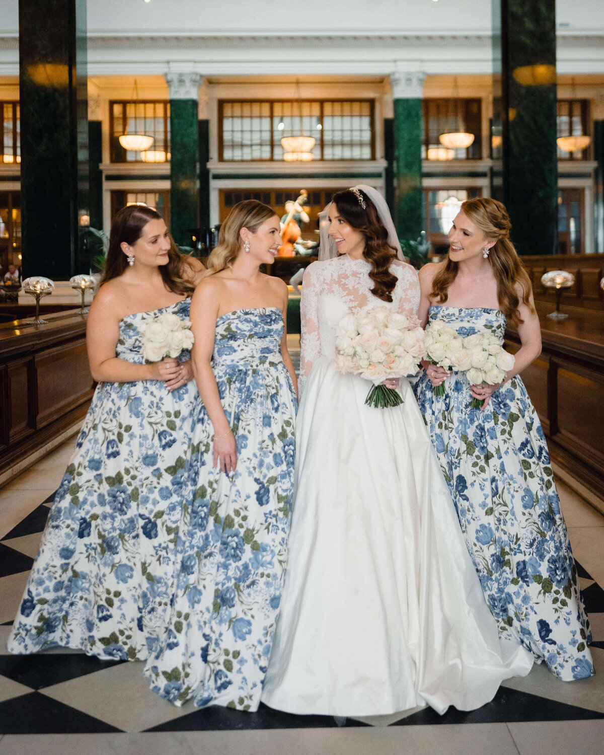 bride walking through the lobby of the ned london with her bridesmaids who all wear blue and green patterned dresses for this chic city wedding