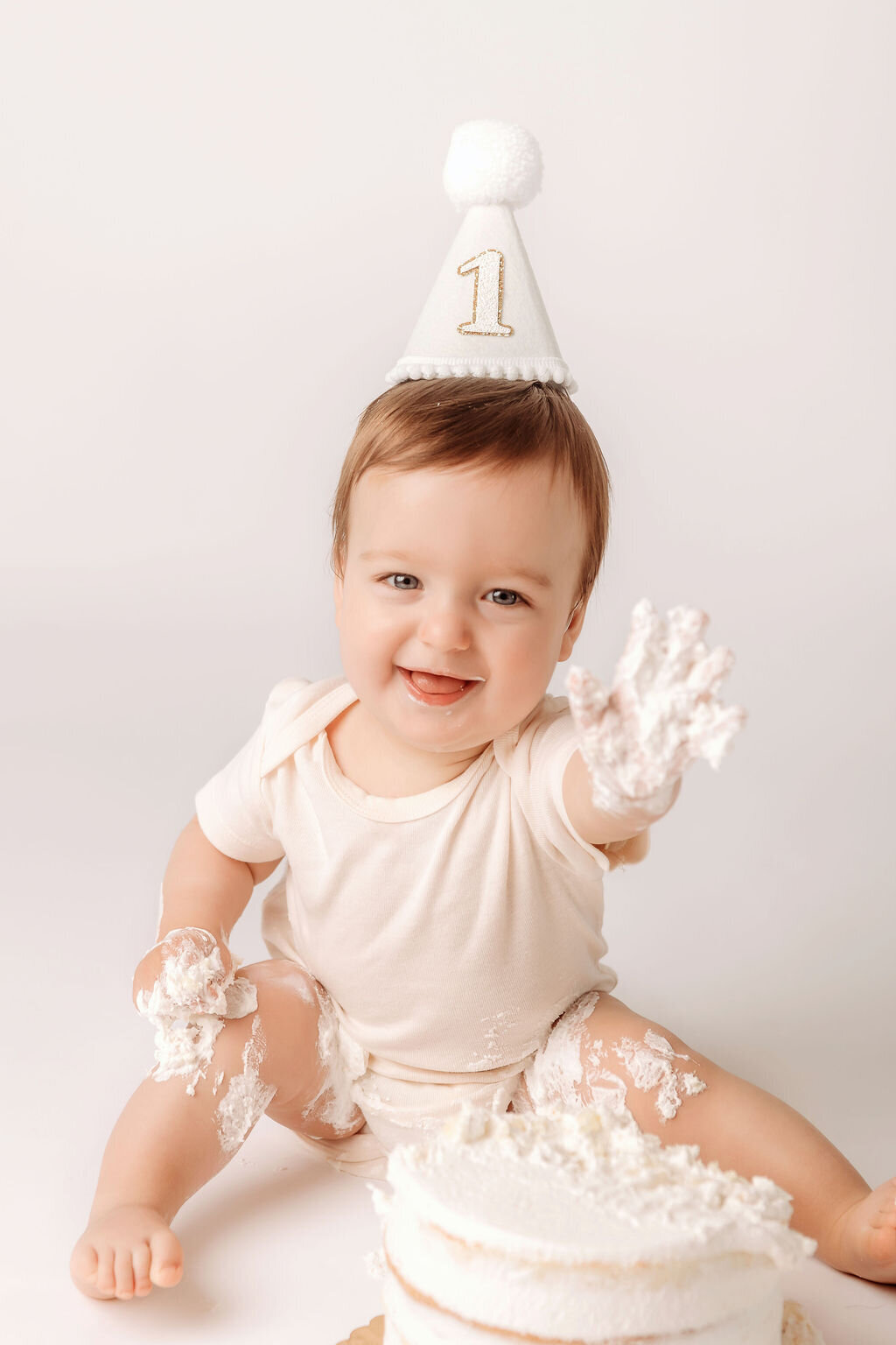 Portrait Photographers CT document joyful cake smash moment as baby reaches toward camera with frosting covered hands wearing golden number one party hat