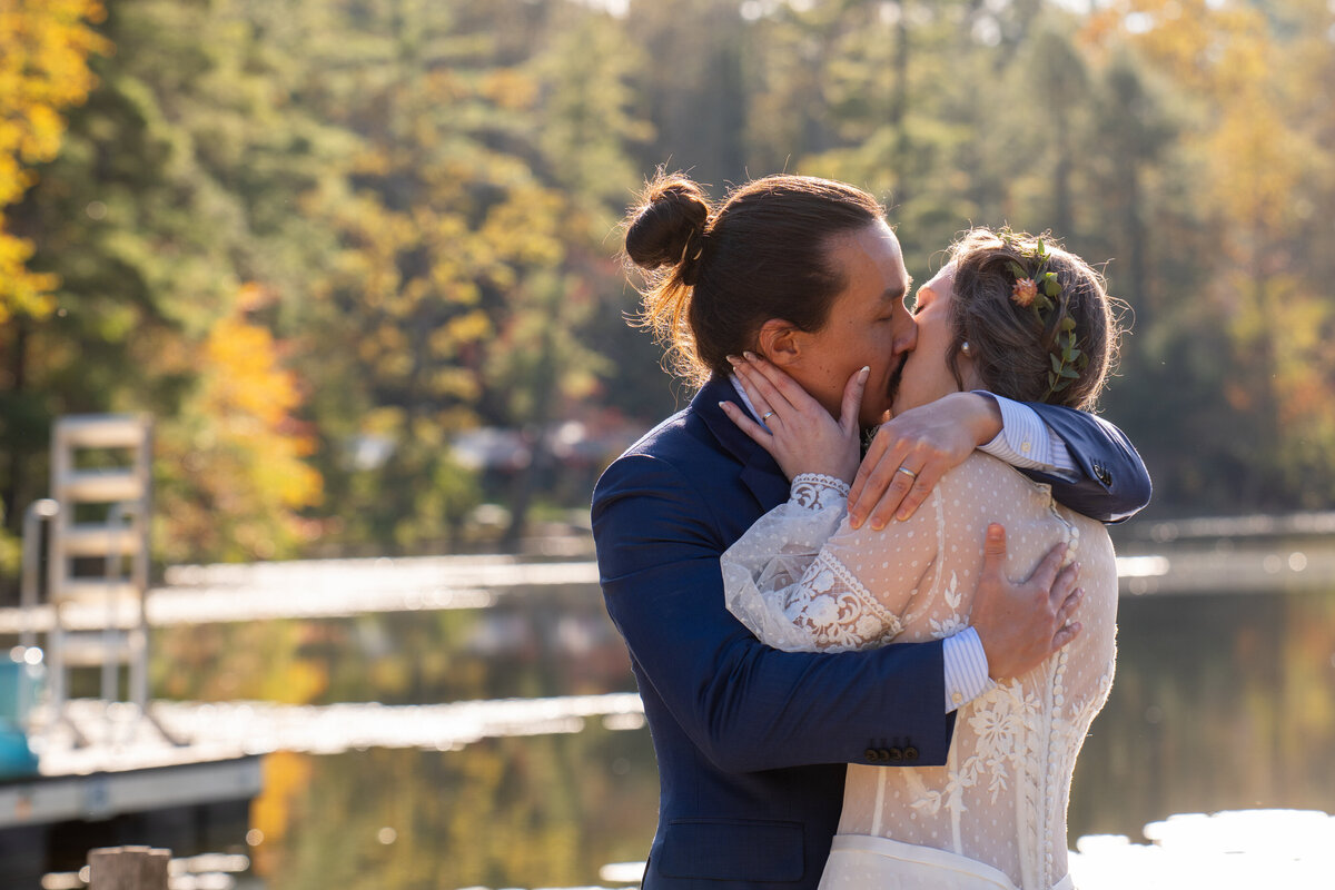 A newlywed couple kissing in front of a lake 