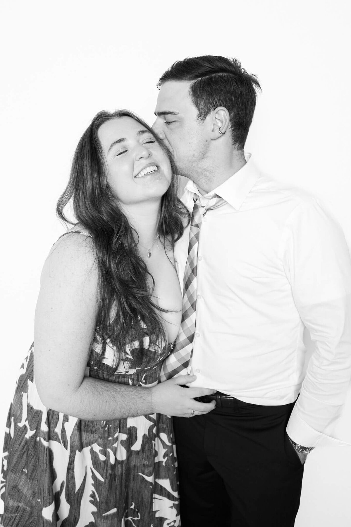 A candid black and white portrait of a couple sharing a kiss and laughing, taken by Monochrome Portraits — a Phoenix photo booth specializing in modern, timeless images.