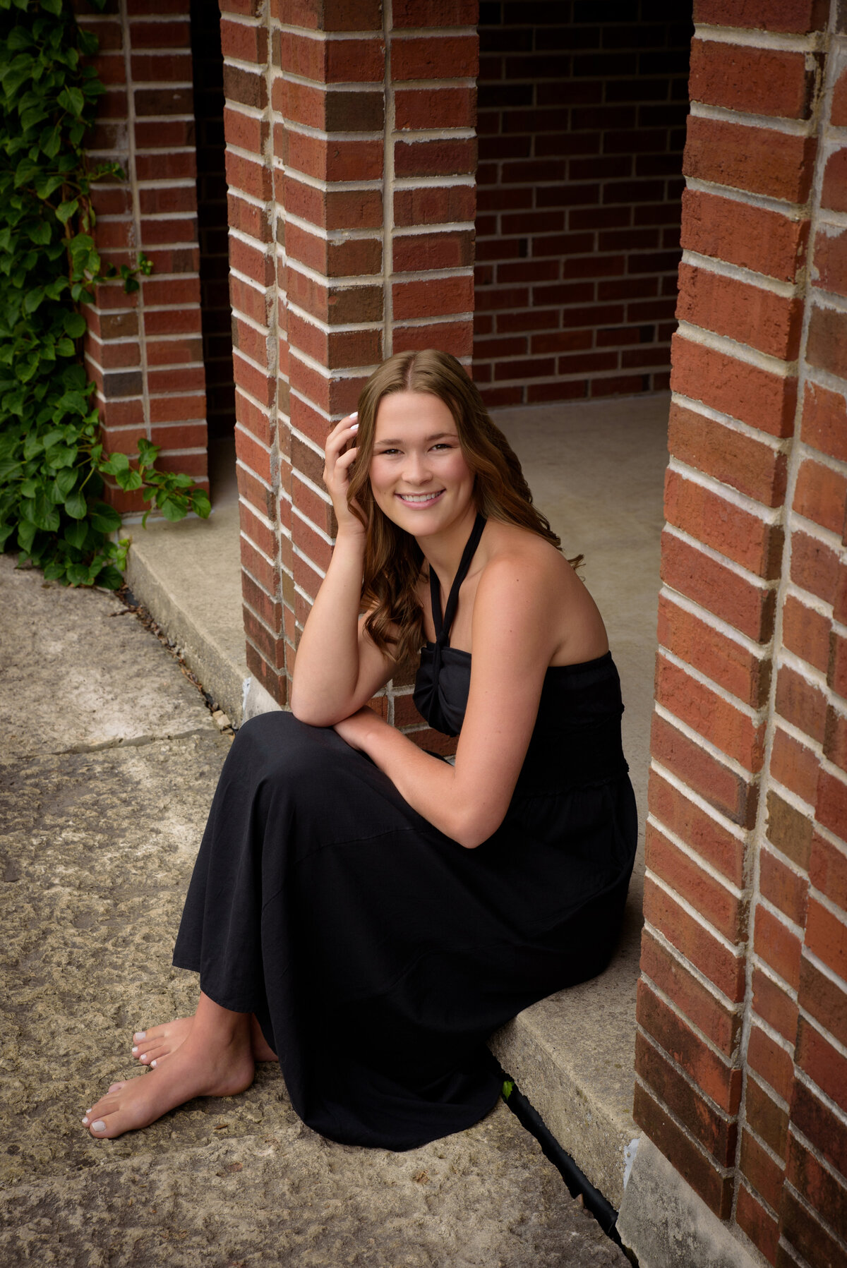 Luxemburg Casco High School senior girl wearing a long black dress by red brick at the Green Bay Botanical Gardens in Green Bay, Wisconsin