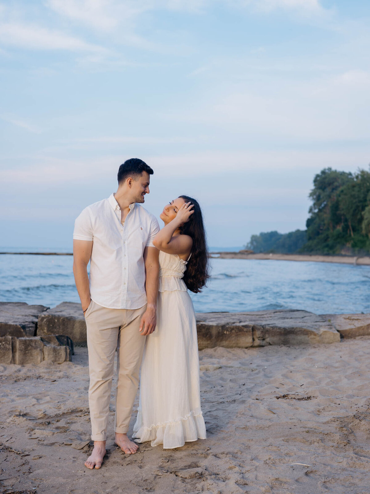 Candid moment of bride running her hand through her hair next to her groom during their lakeside beach engagement session.