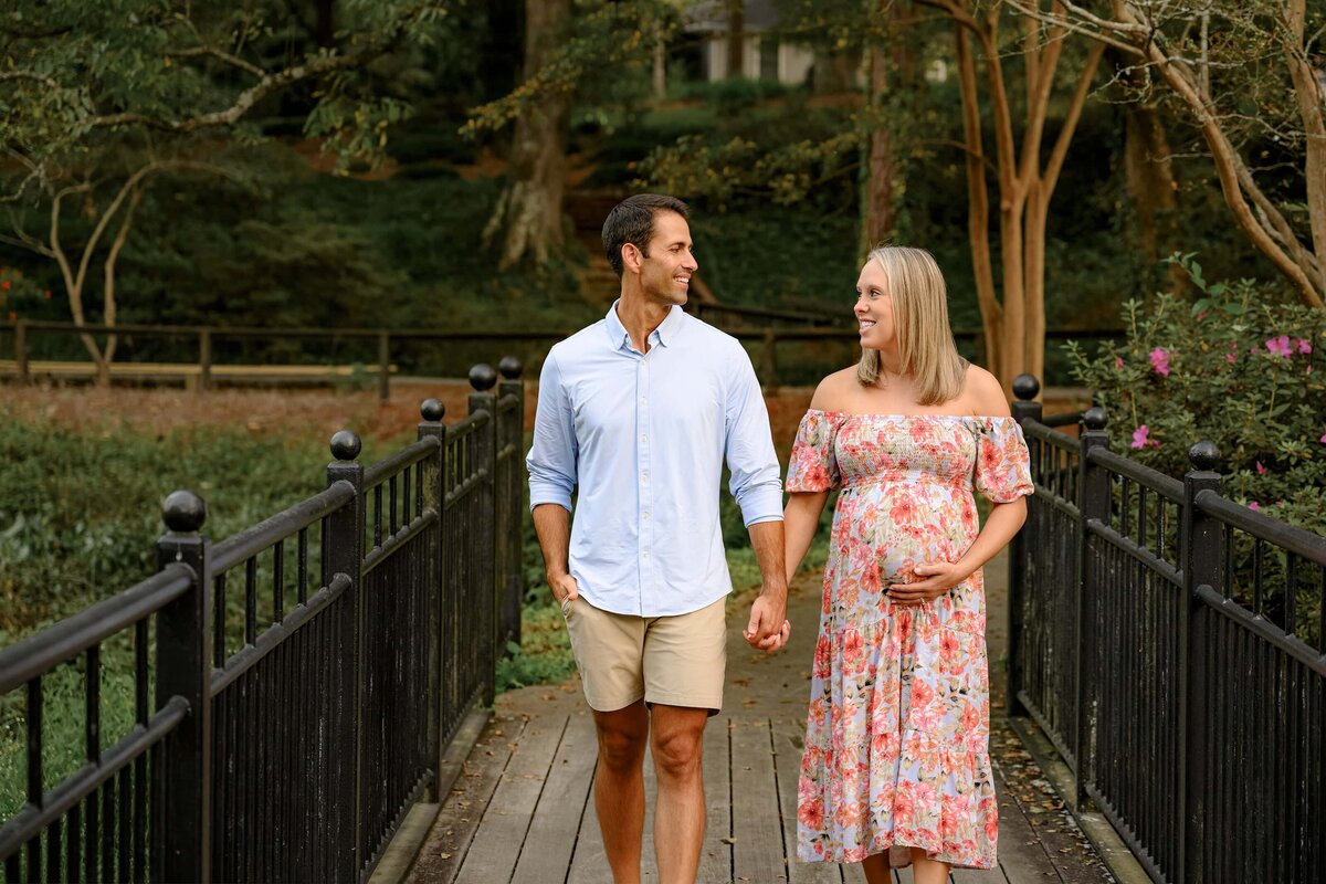 couple expecting their first child holds hands and walks together across a bridge during their maternity session