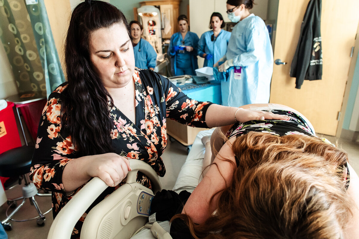 A surrogate groans in pain while the mom-to-be rubs her back during a contractin