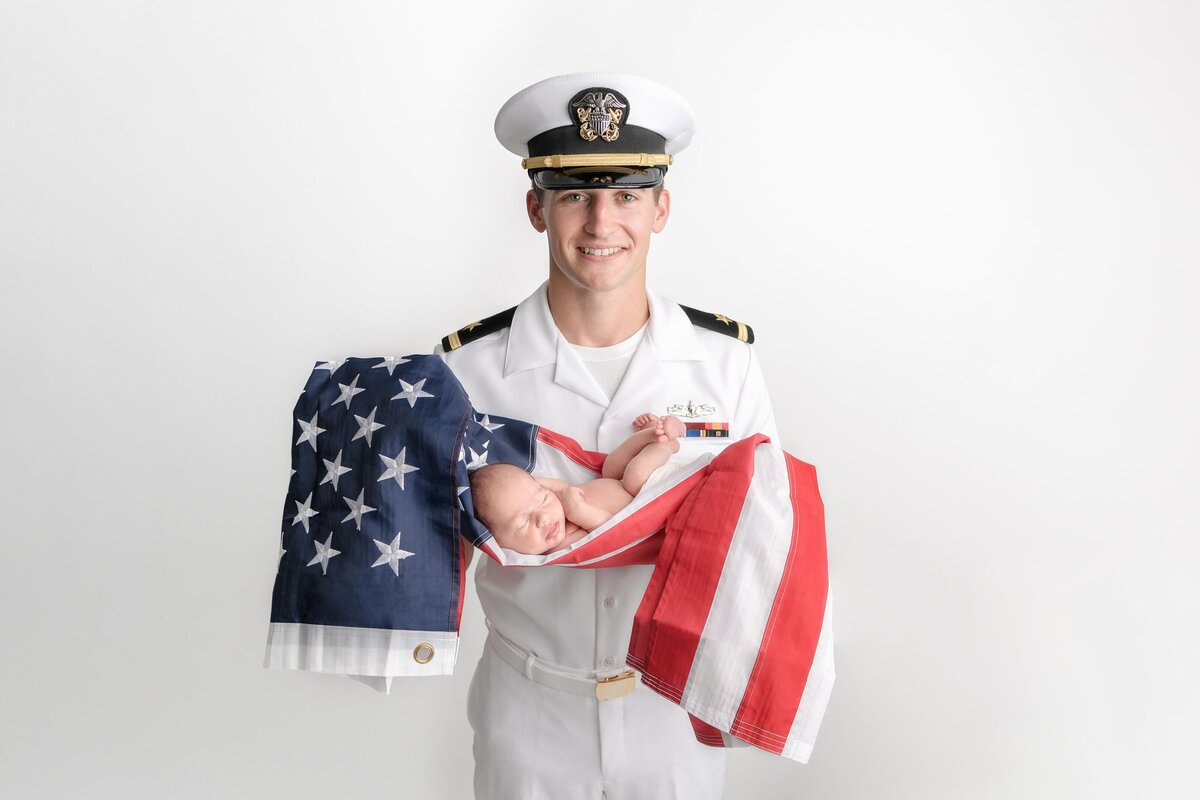 New Dad Dressed In Air Force Uniform Holding Newborn Son Craddled In American Flag
