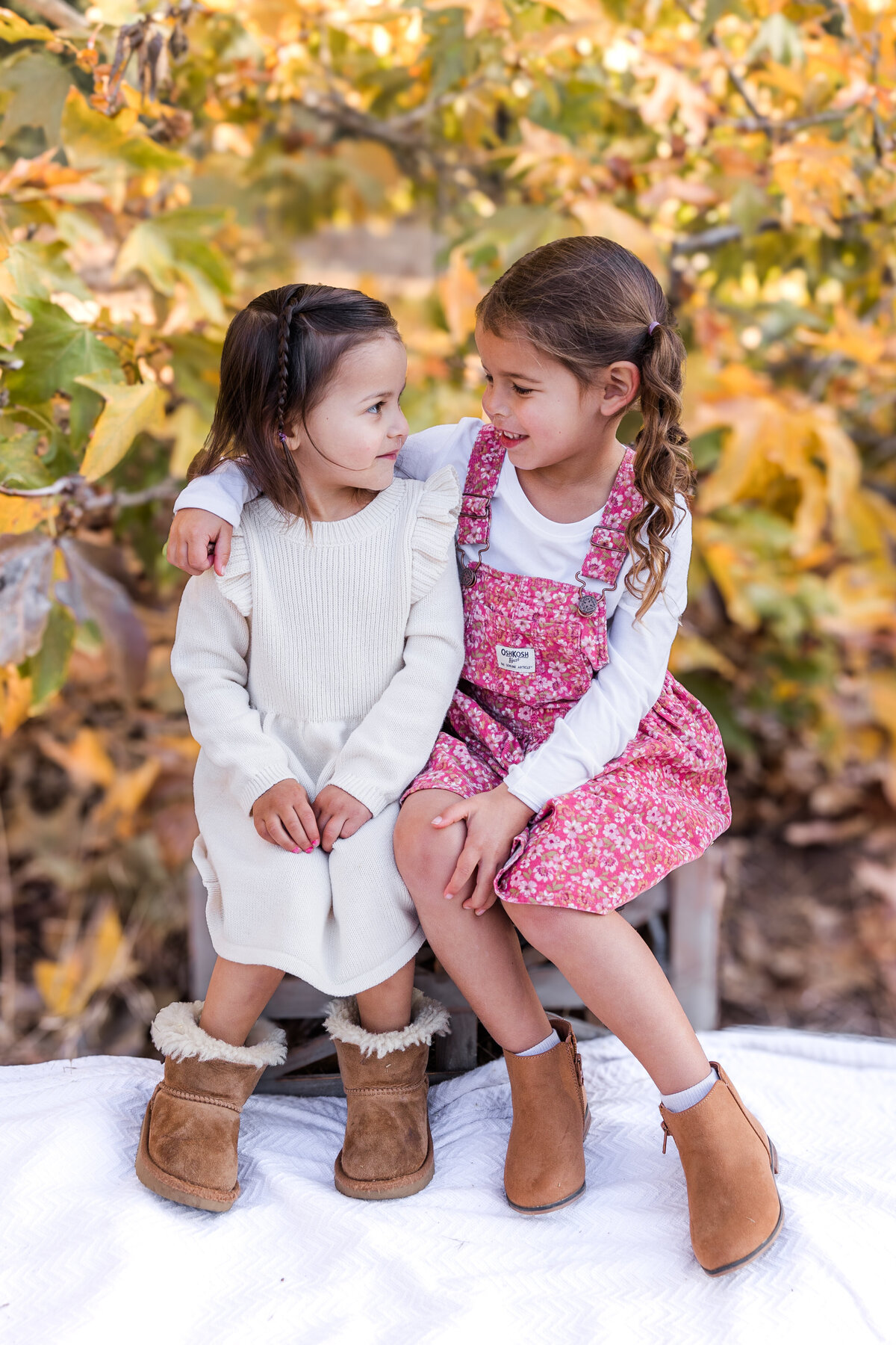 sisters sitting on crate by fall leaves