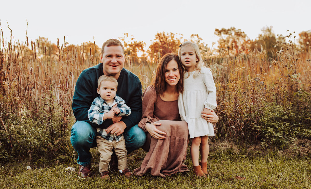 family of 4, looking at the camera. field behind them,