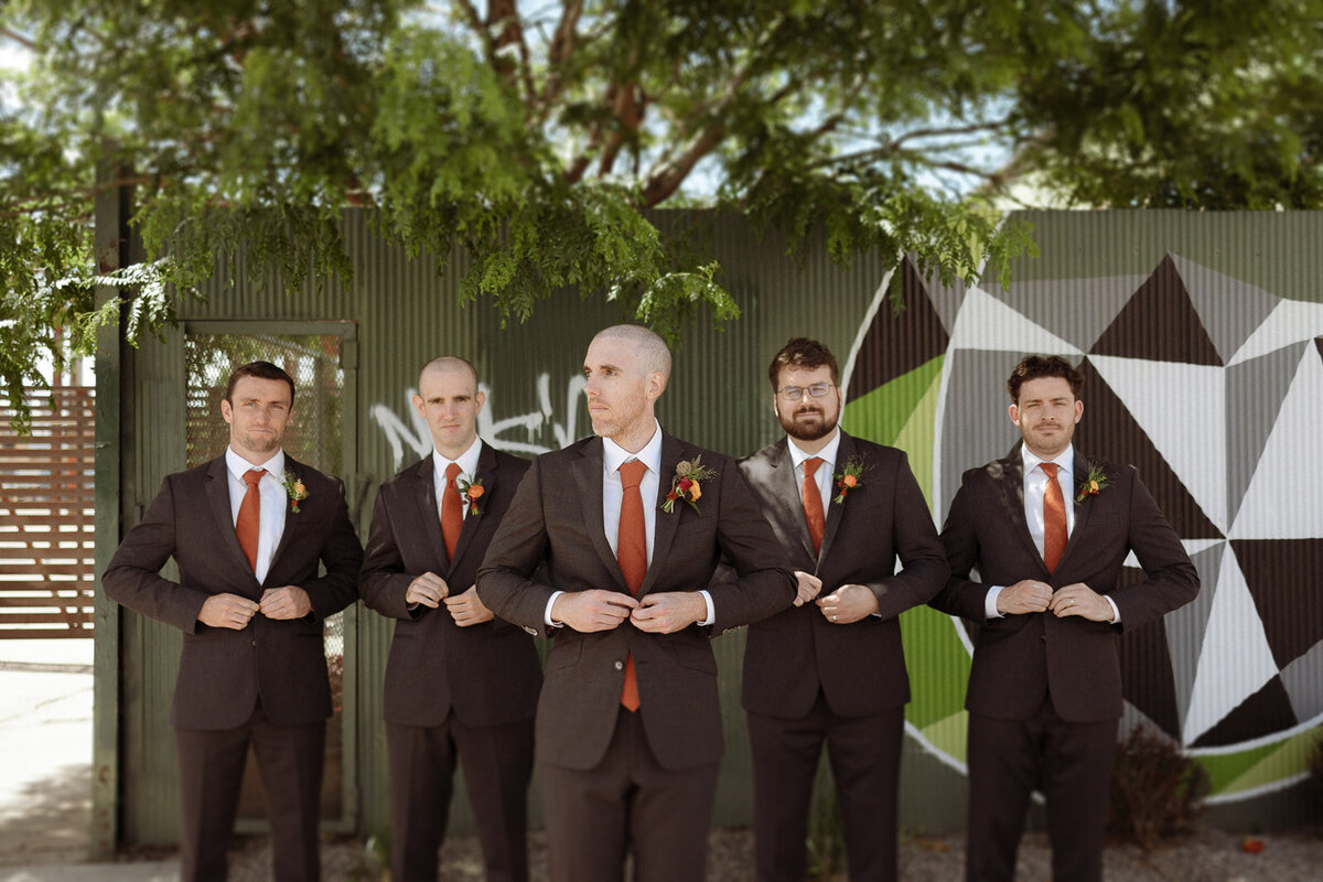 Groom and groomsmen pose in black suits with red accents.