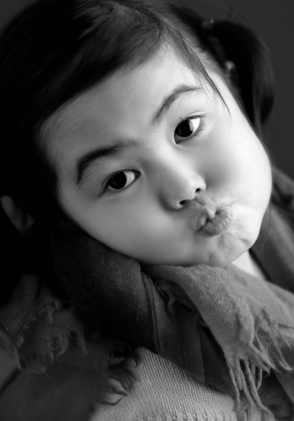 A little girl wearing a colorful scarf on her neck, making silly faces at the camera.