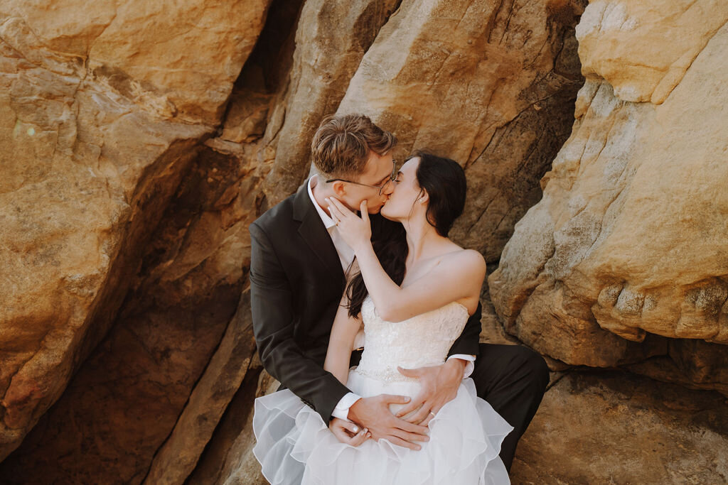 a bride and groom kissing by a rock wall