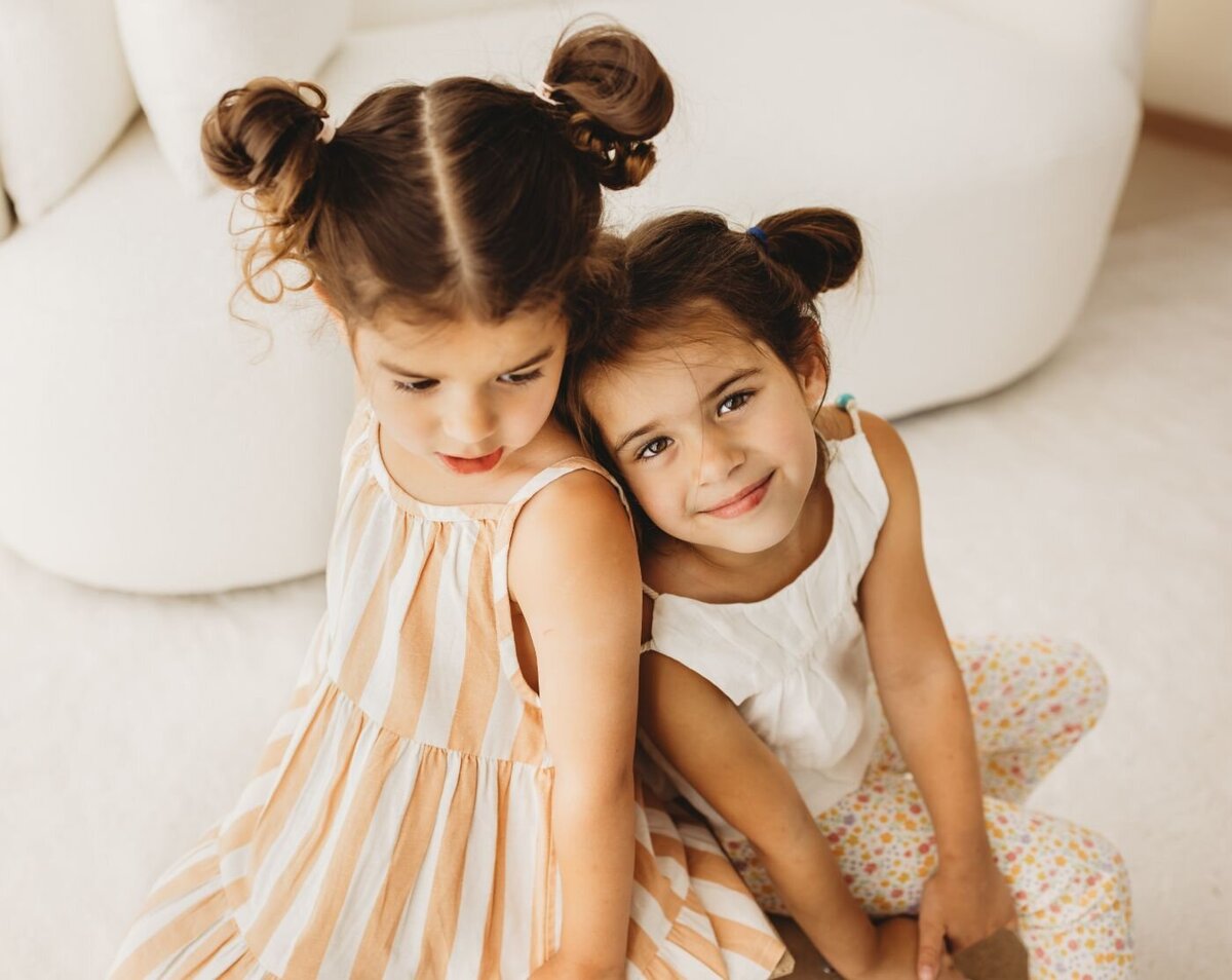 two sisters sitting next to each other on their backs ans the small one is looking at the camera smiling and the big sister is looking down