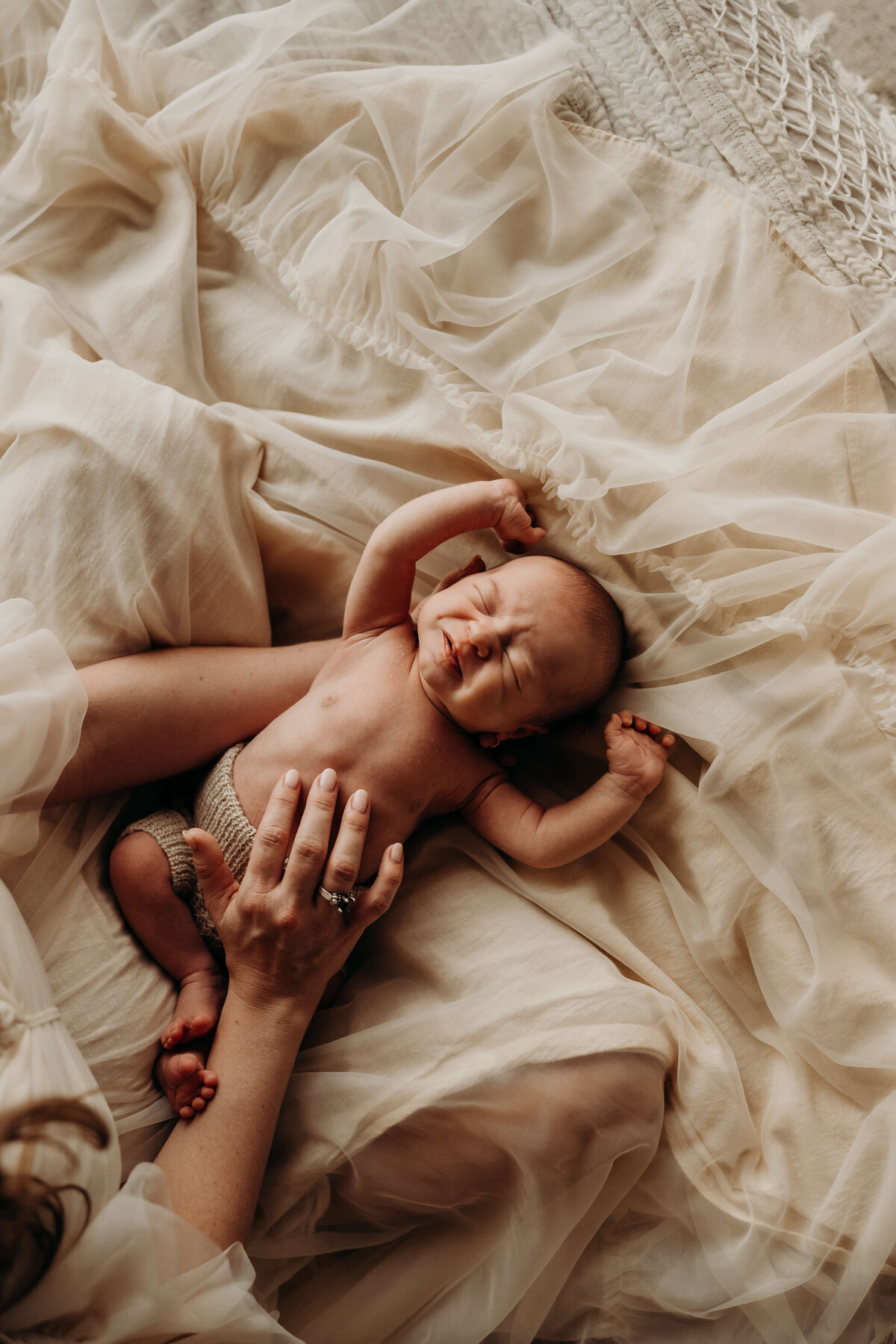 newborn baby boy yawns on bed while being held by his mom