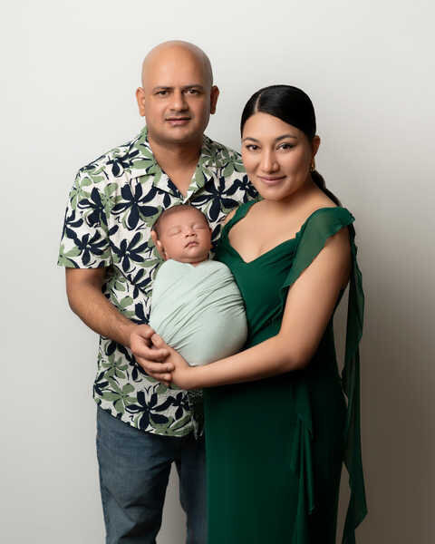 Parents holding newborn baby swaddled in green wrap during Houston family photography session.