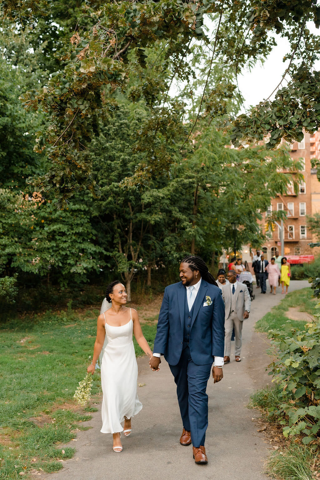 bride and groom holding hands and looking at each other as they lead a group of guests along a path