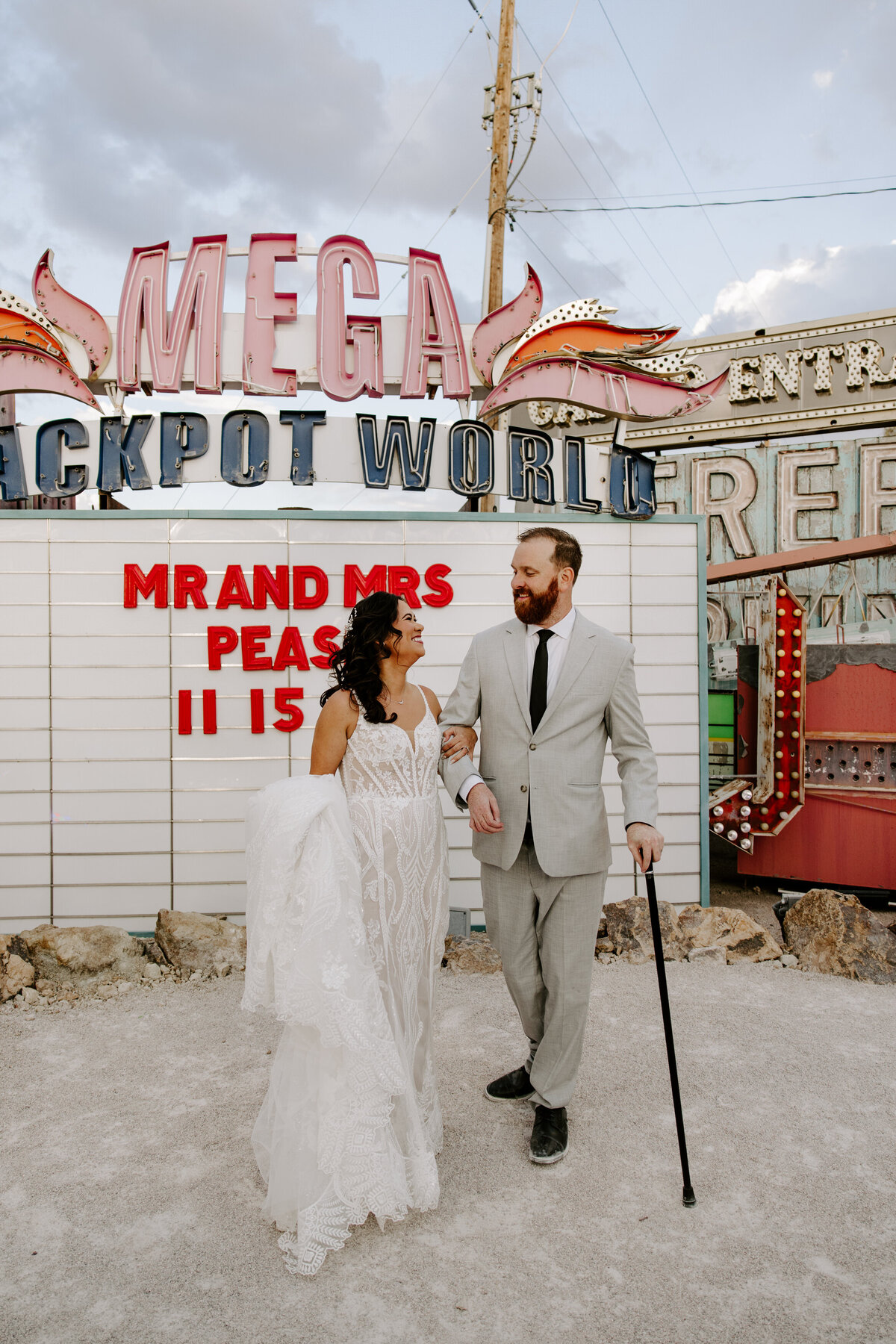 Two people pose in front of a sign that says Mega Jackpot World during their Neon Museum wedding in Vegas.