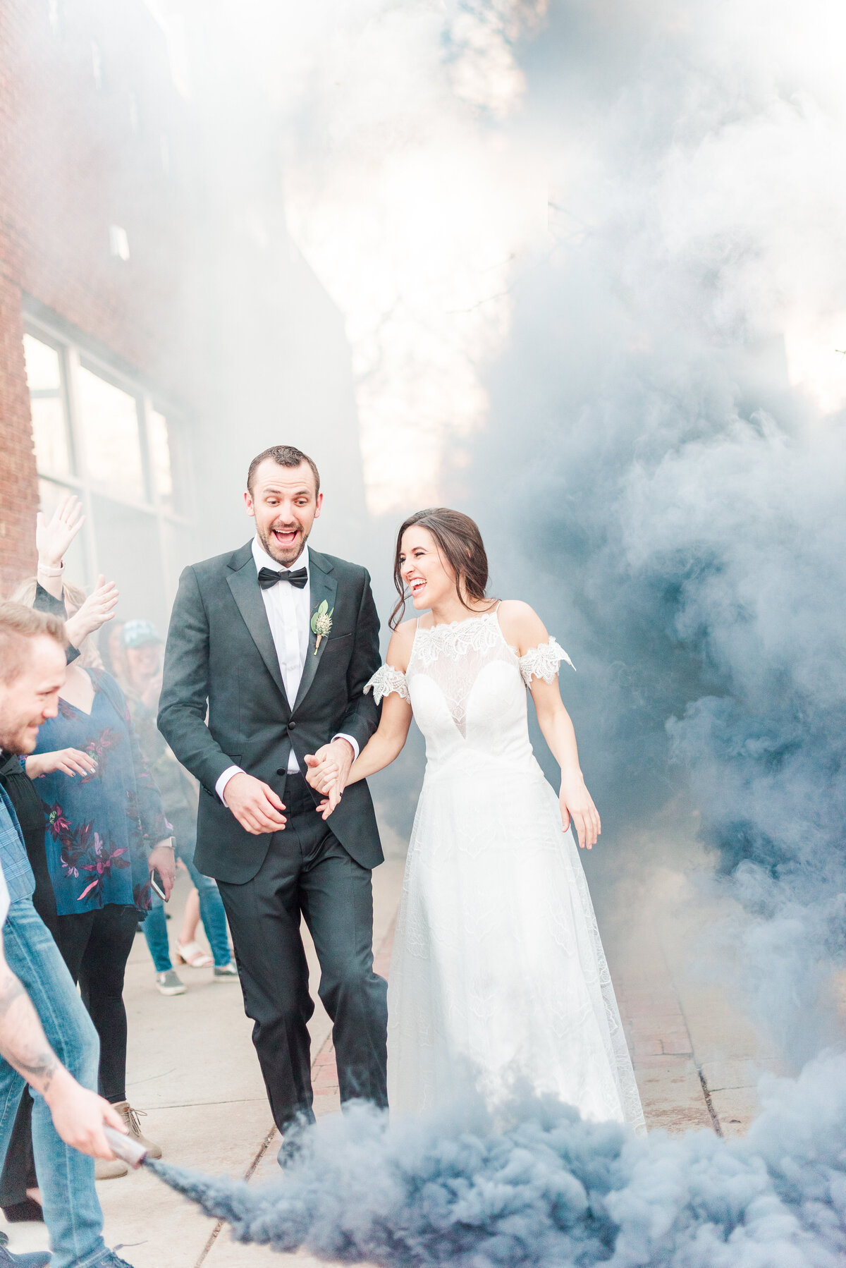 unique bride and groom exit with blue smoke bombs as the bride and groom hold hands as they walk past their friend and family at the st. vrain wedding venue