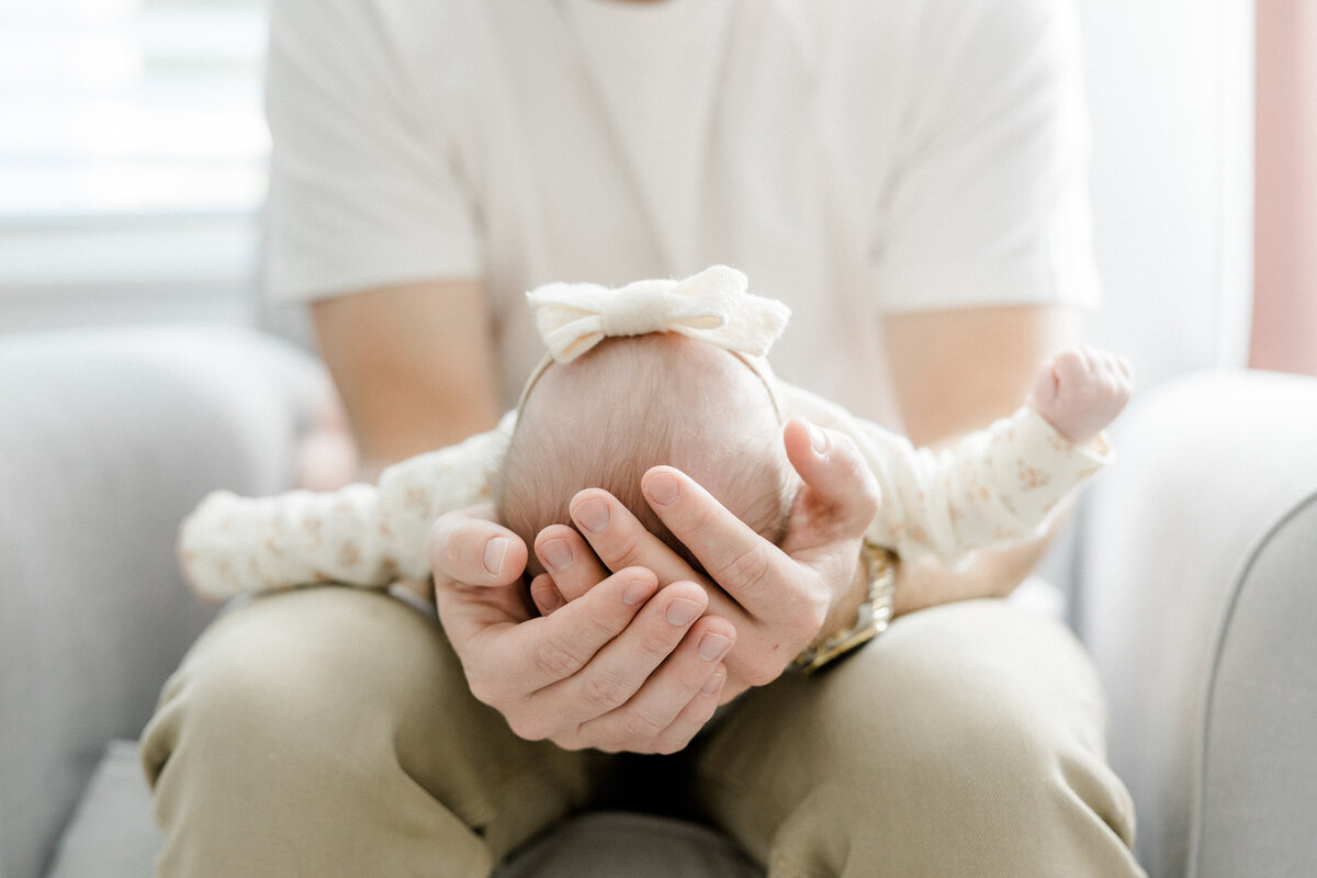 dad's hands wrapped around baby's head during newborn session