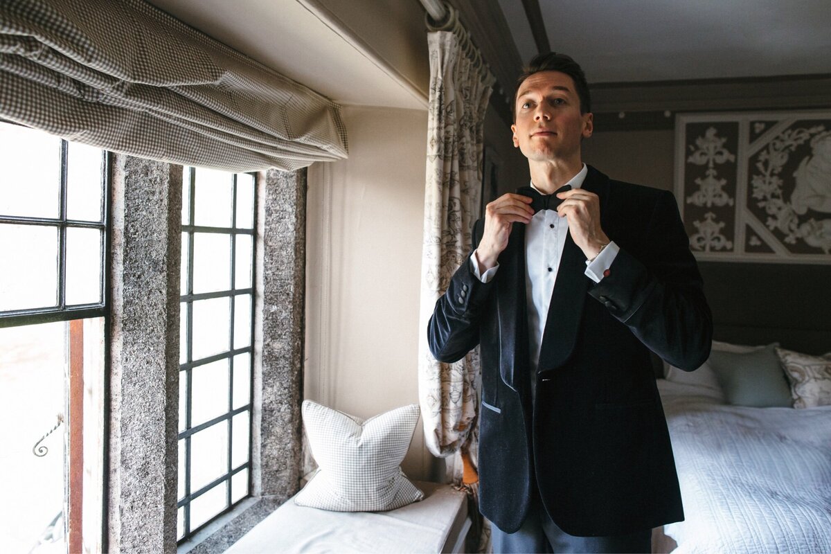 Groom adjusts bow tie wearing velvet jacket