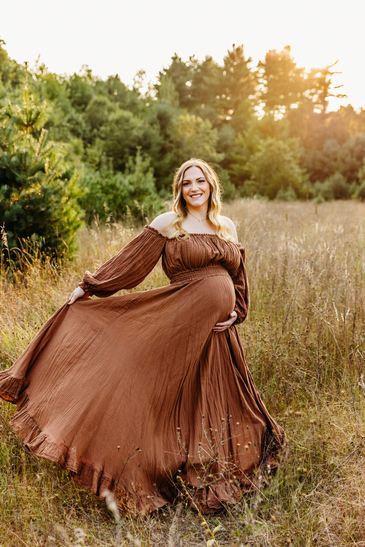 stunning mother to be in a light brown dress twirling and smiling as the sun is setting behind her for her maternity photo session