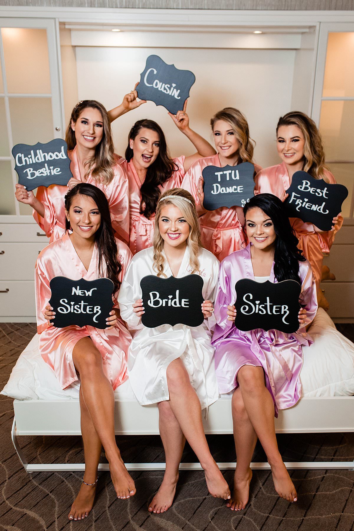 Bridesmaids holding signs showing how they know the bride while wearing robes