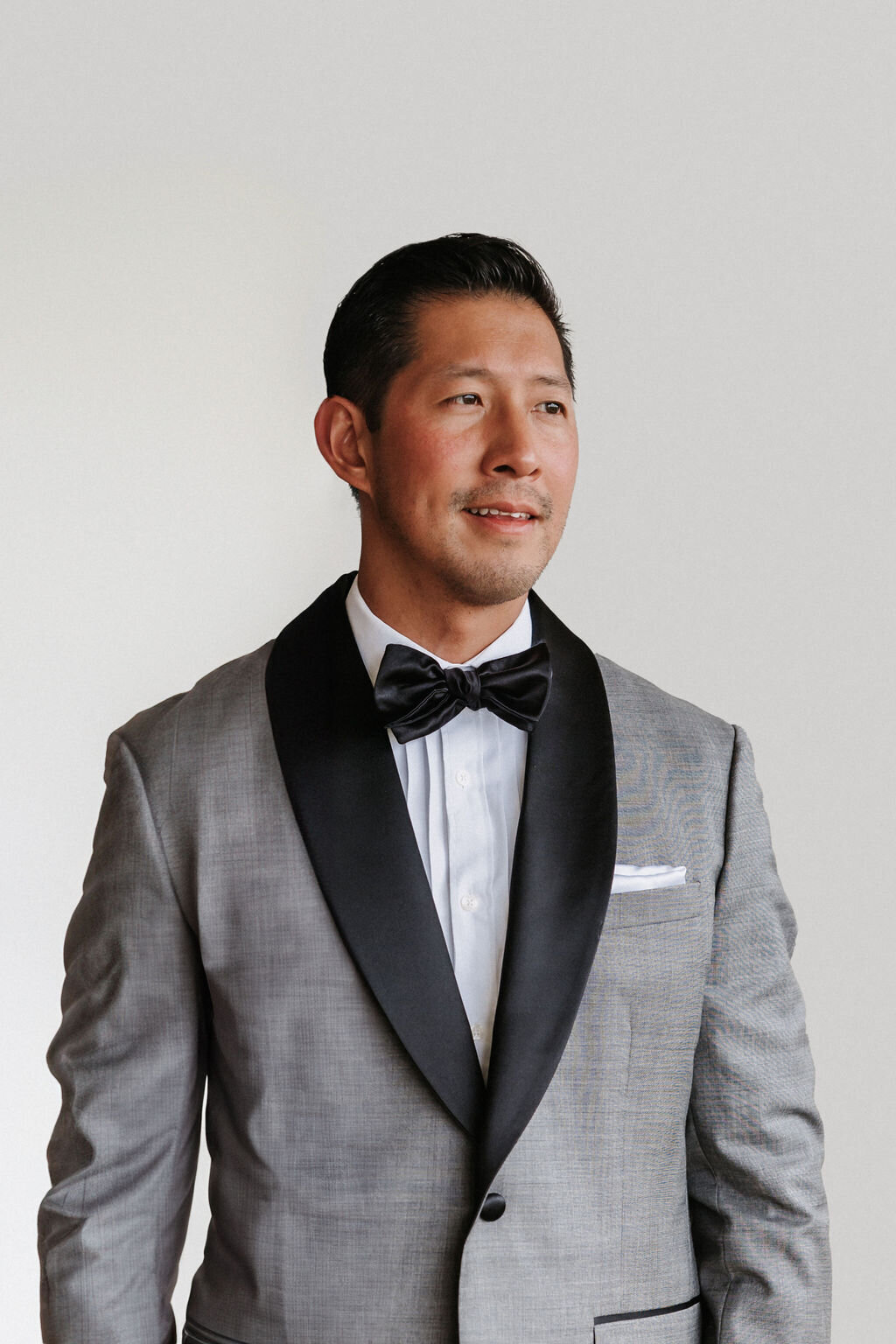 groom portrait wearing grey tuxedo against white backdrop by hawaii wedding photographer