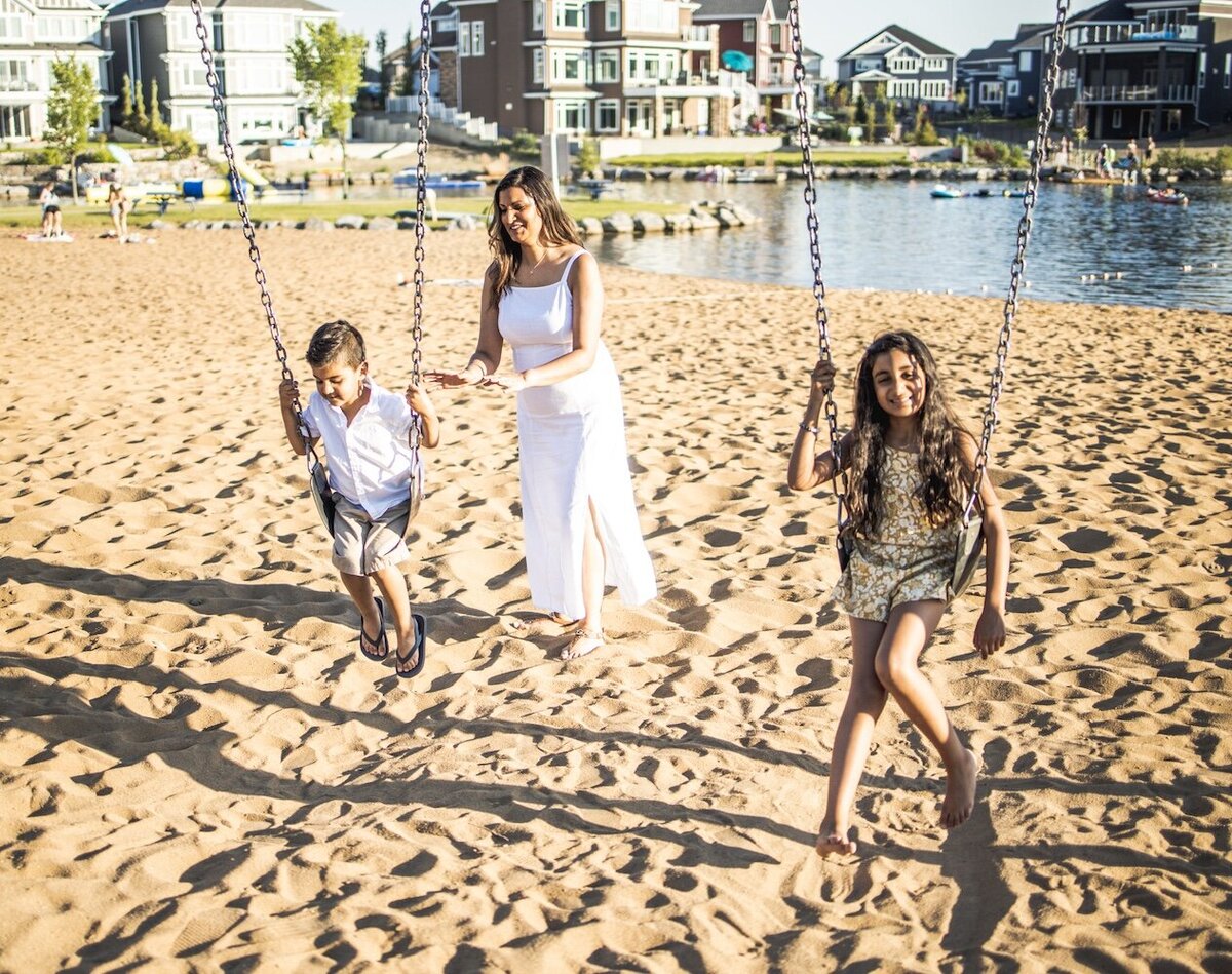 Mom in a white dress pushing her son and daughter on a swing 