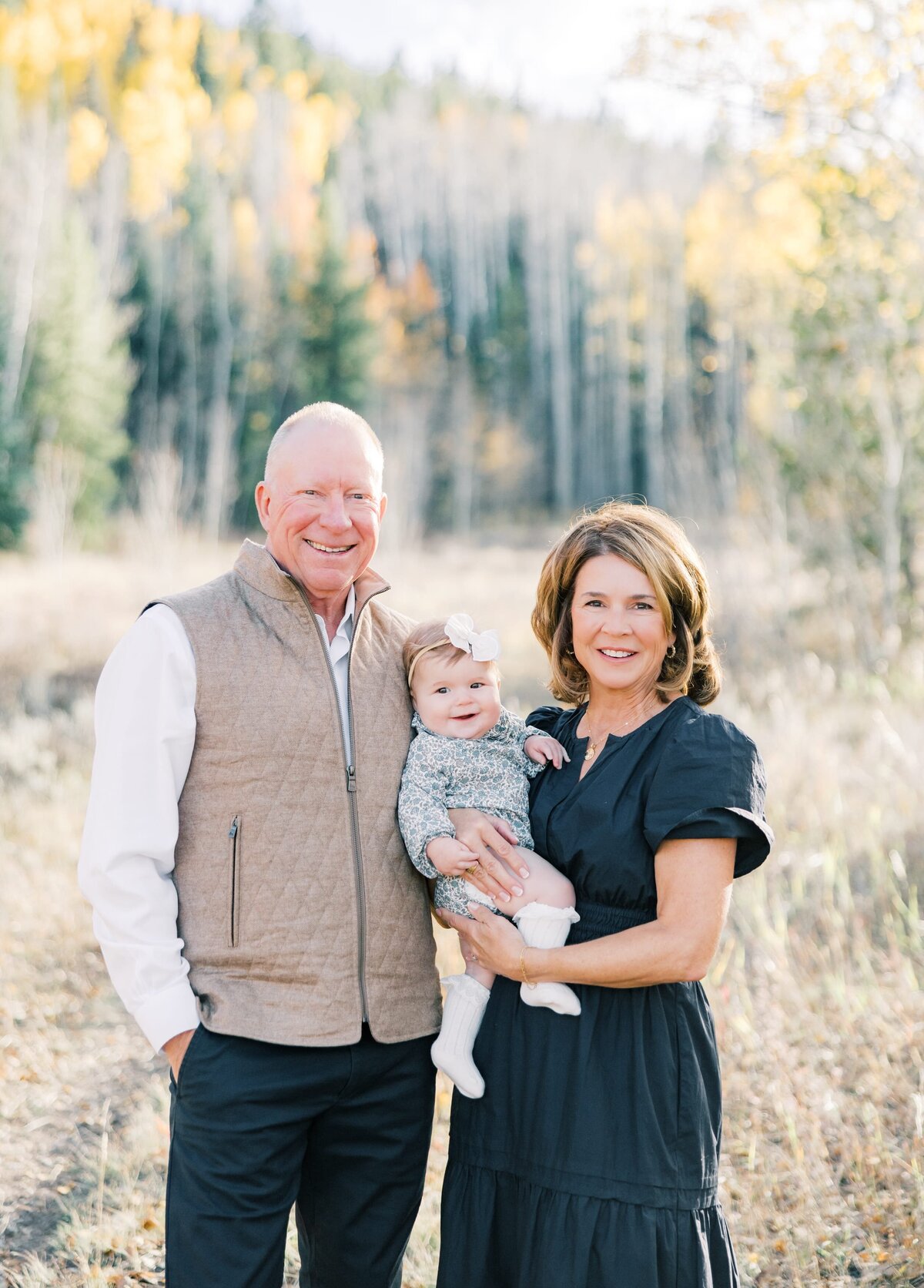 The grandma and grandpa are holding their young grandchild in their arms while she smiles at the camera. Taken by a local Breckenridge photographer. 