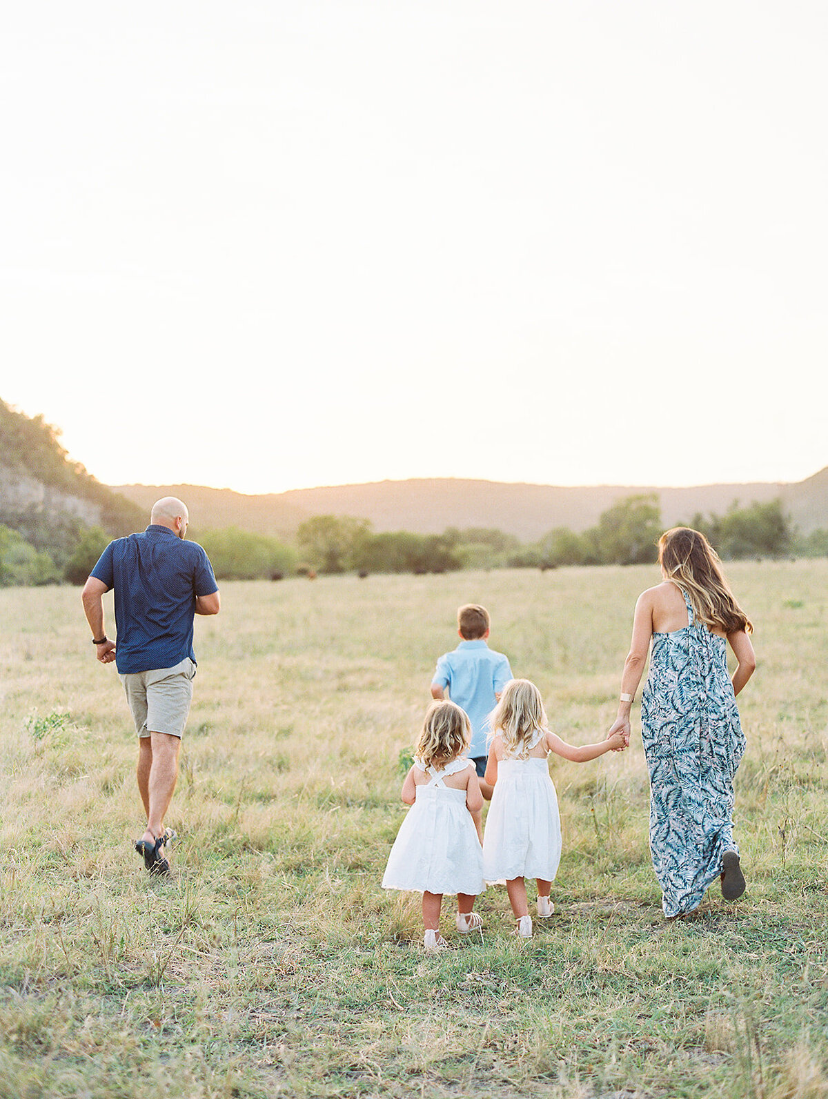 Family of five holding hands and running through a grassy field