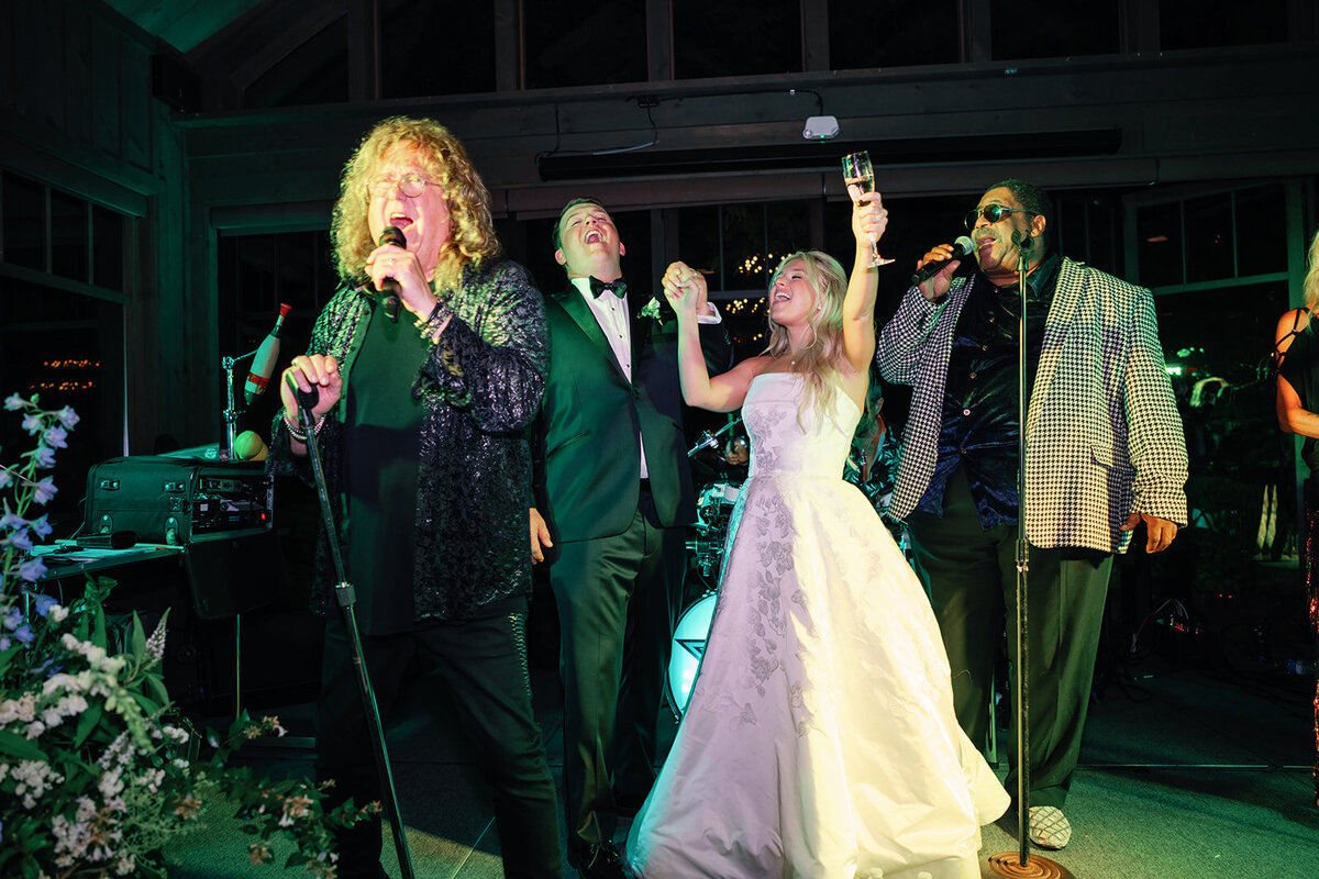 Bride and groom celebrate on stage with a live band during a lively wedding reception in Highlands, NC.