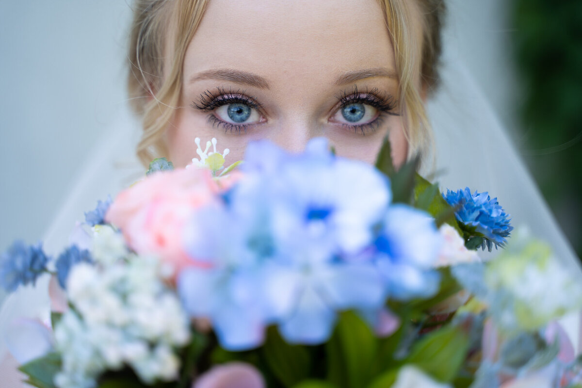 The beautiful bride, Keira, peaking her blue eyes out from behind her bouquet at her intimate church wedding in Delaware, Ohio.