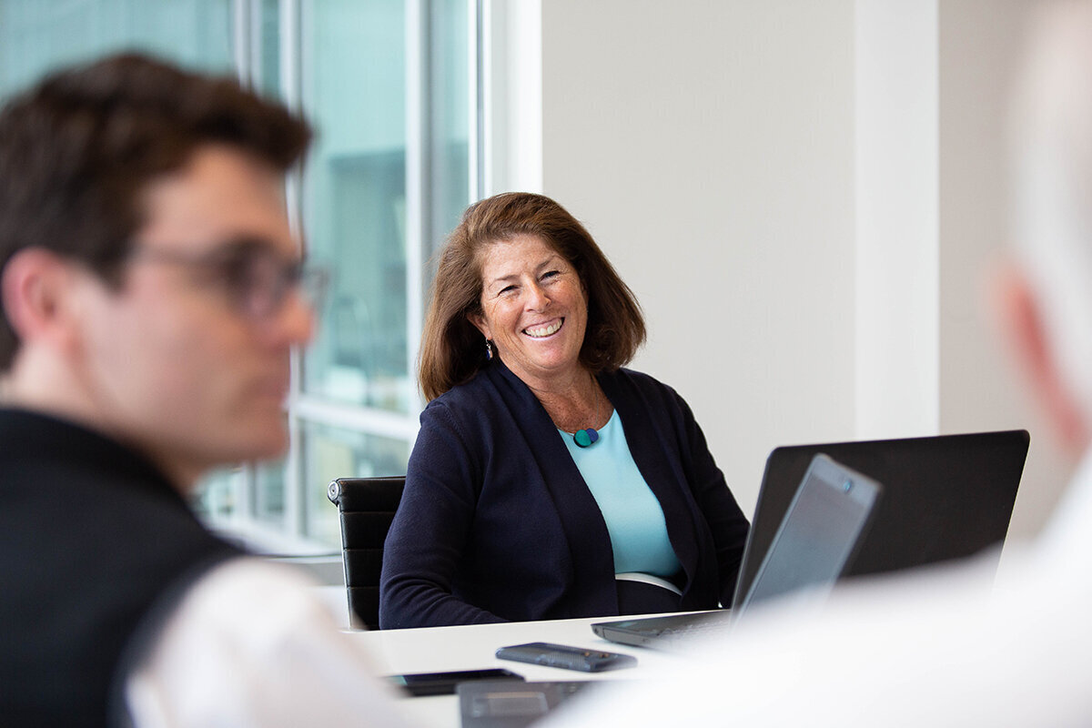 Businesswoman laughing in a glass walled conference room with our of focus men in the foreground
