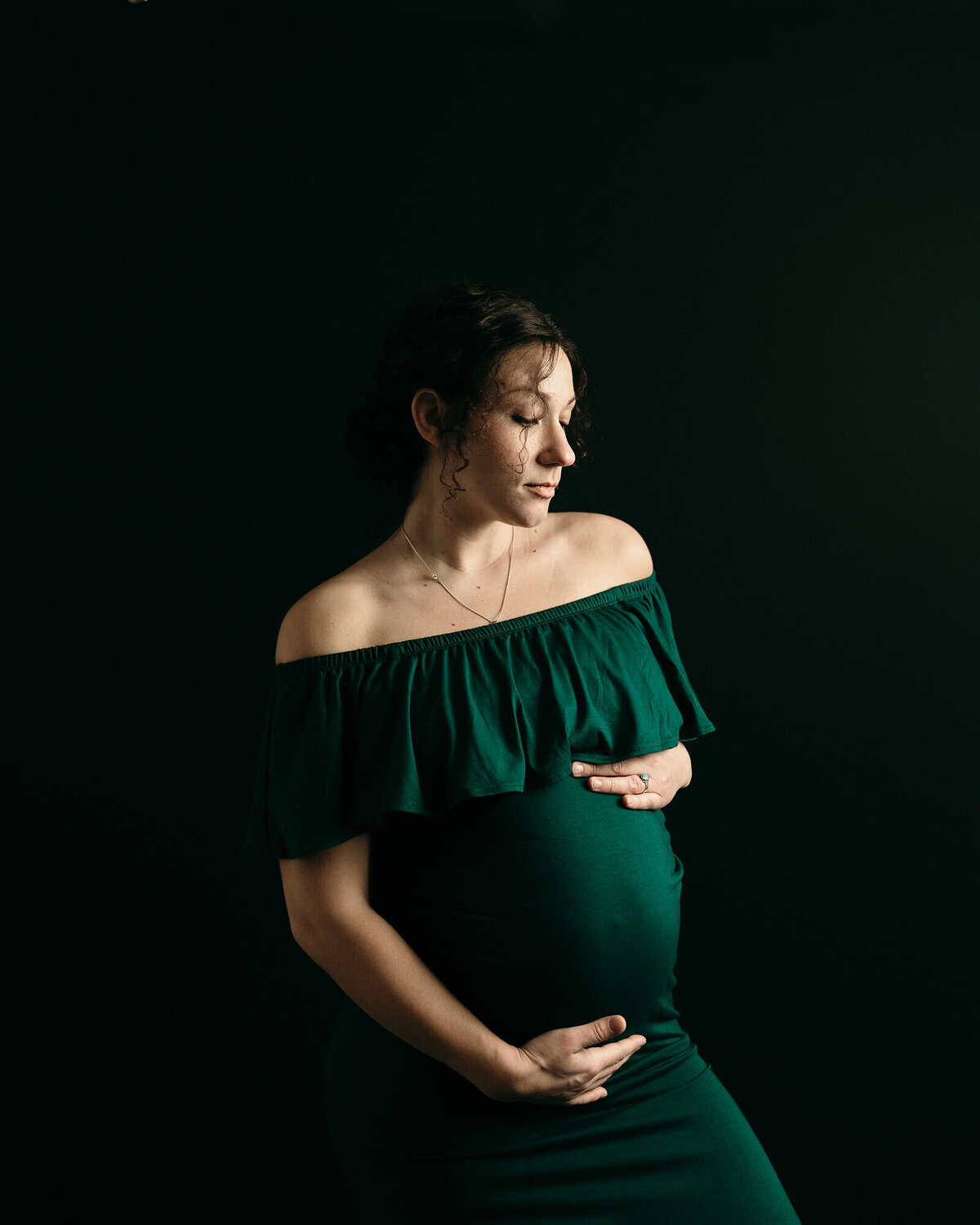 Pregnant woman in green maternity gown holding her belly.