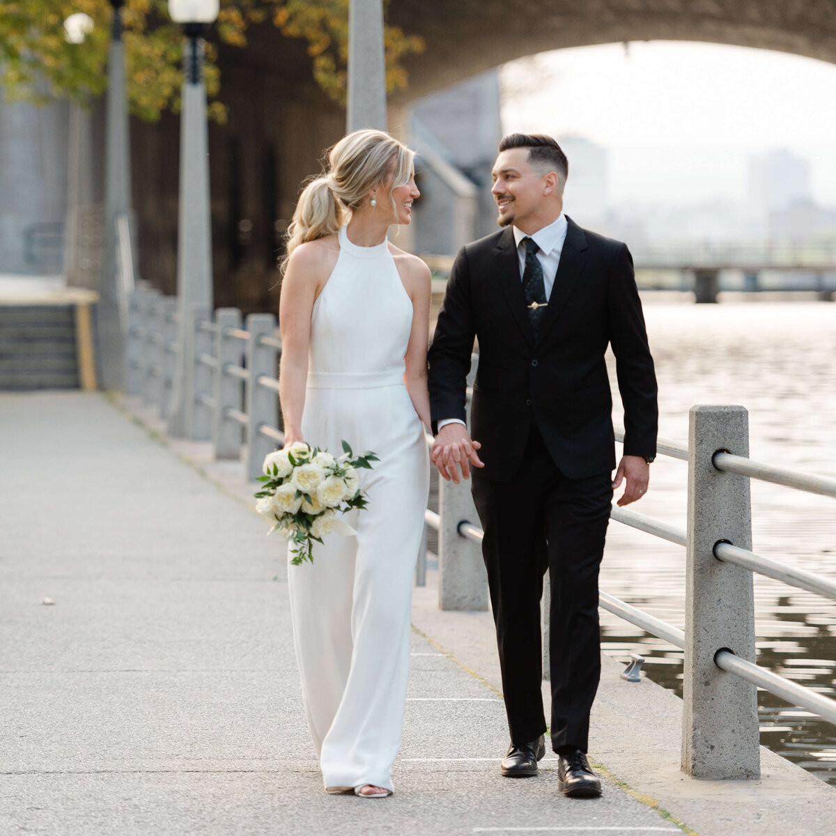 a bride in a pantsuit and a groom in a black suit walking outside the NAC venue taken by Ottawa wedding photographer JEMMAN Photography
