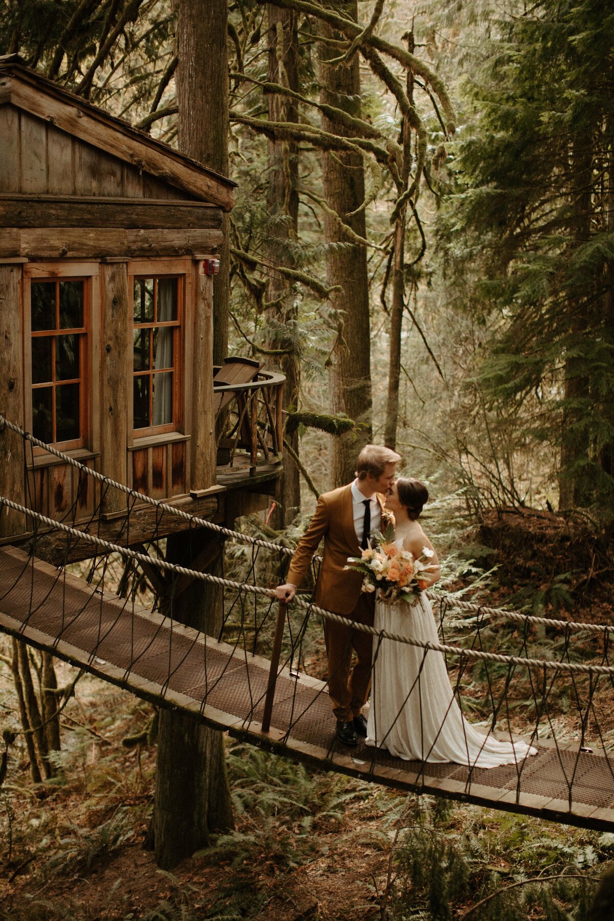 Groom kissing brides forehead on tree house bridge!