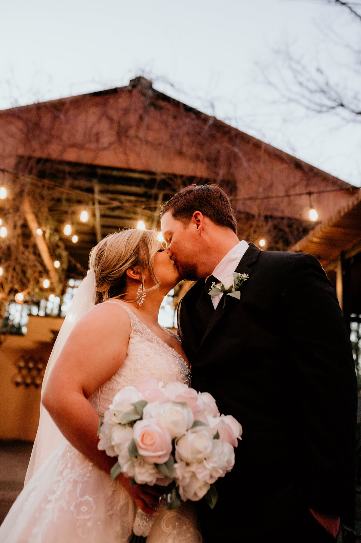 bride and groom kissing under a string of lights at their outdoor wedding venue captured by Little Rock wedding photographer