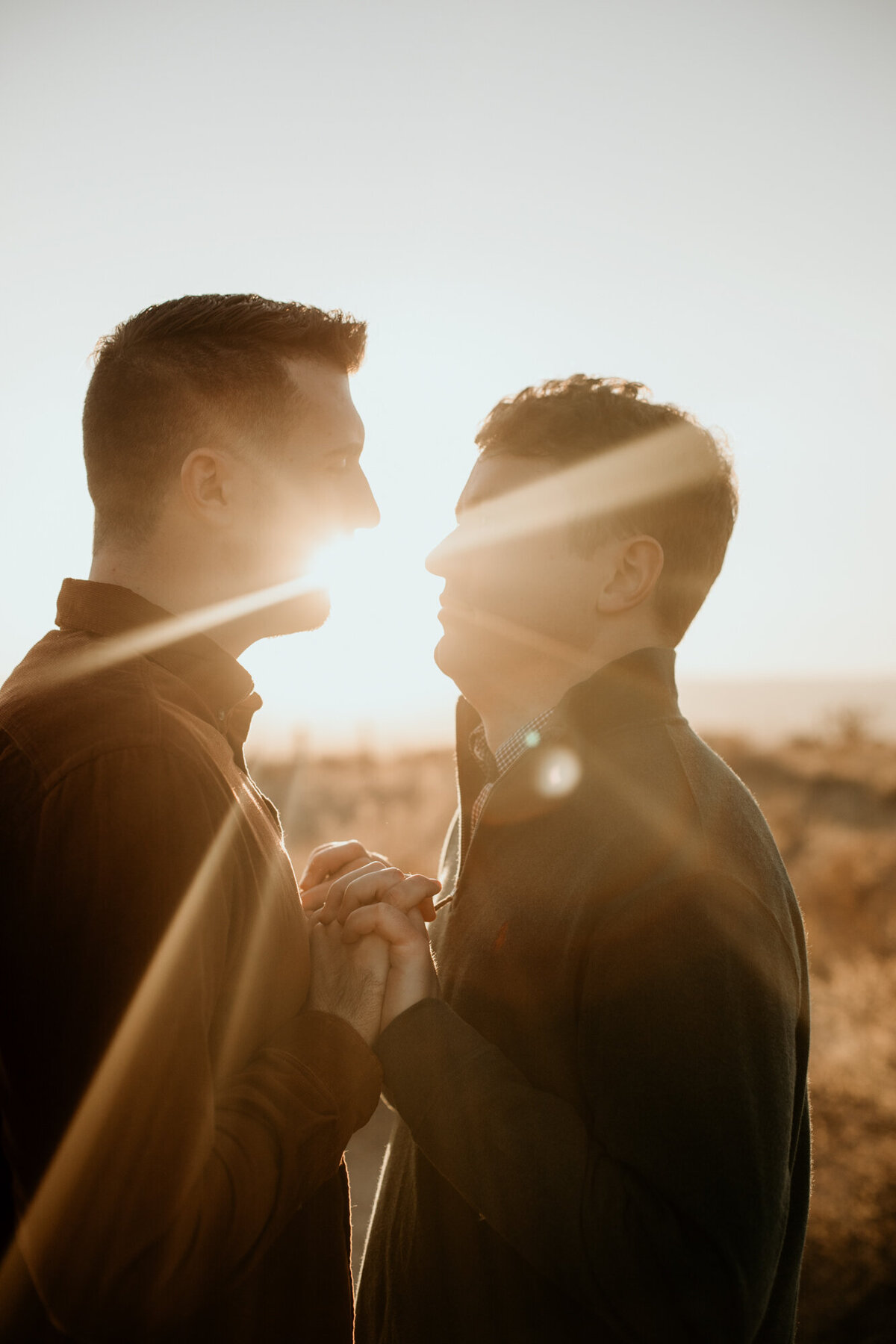 gay couple holding hands looking at each other with sun flare