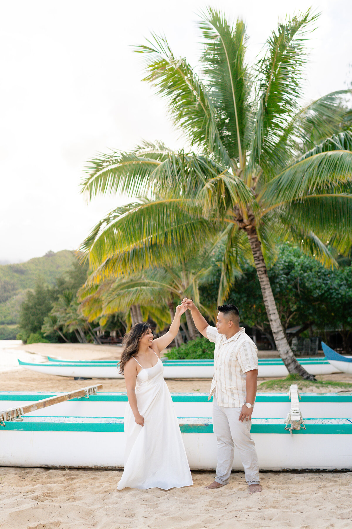 Oahu Hawaii Elopement Asian couple dancing and spinning at Secret Island Beach during sunset with boats and canoes.