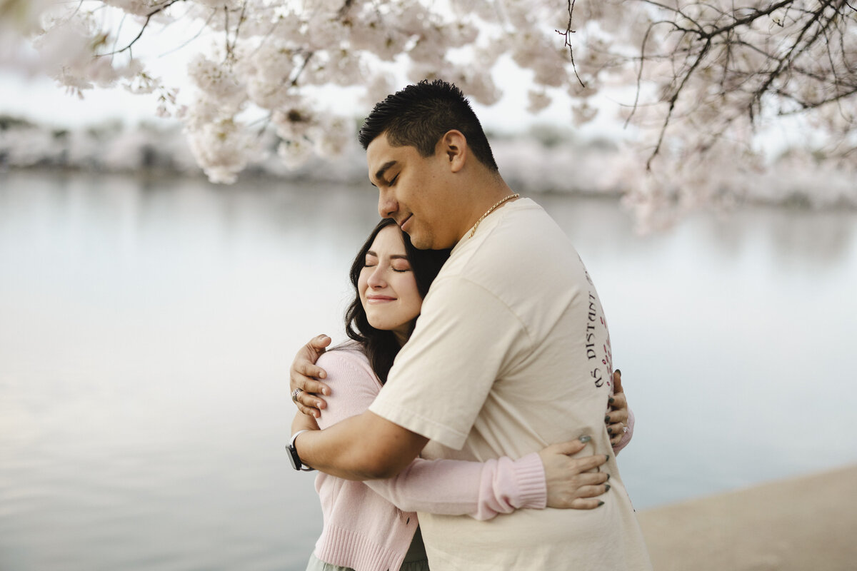 A couple hugs one another surrounded by cherry blossoms in Washington DC.