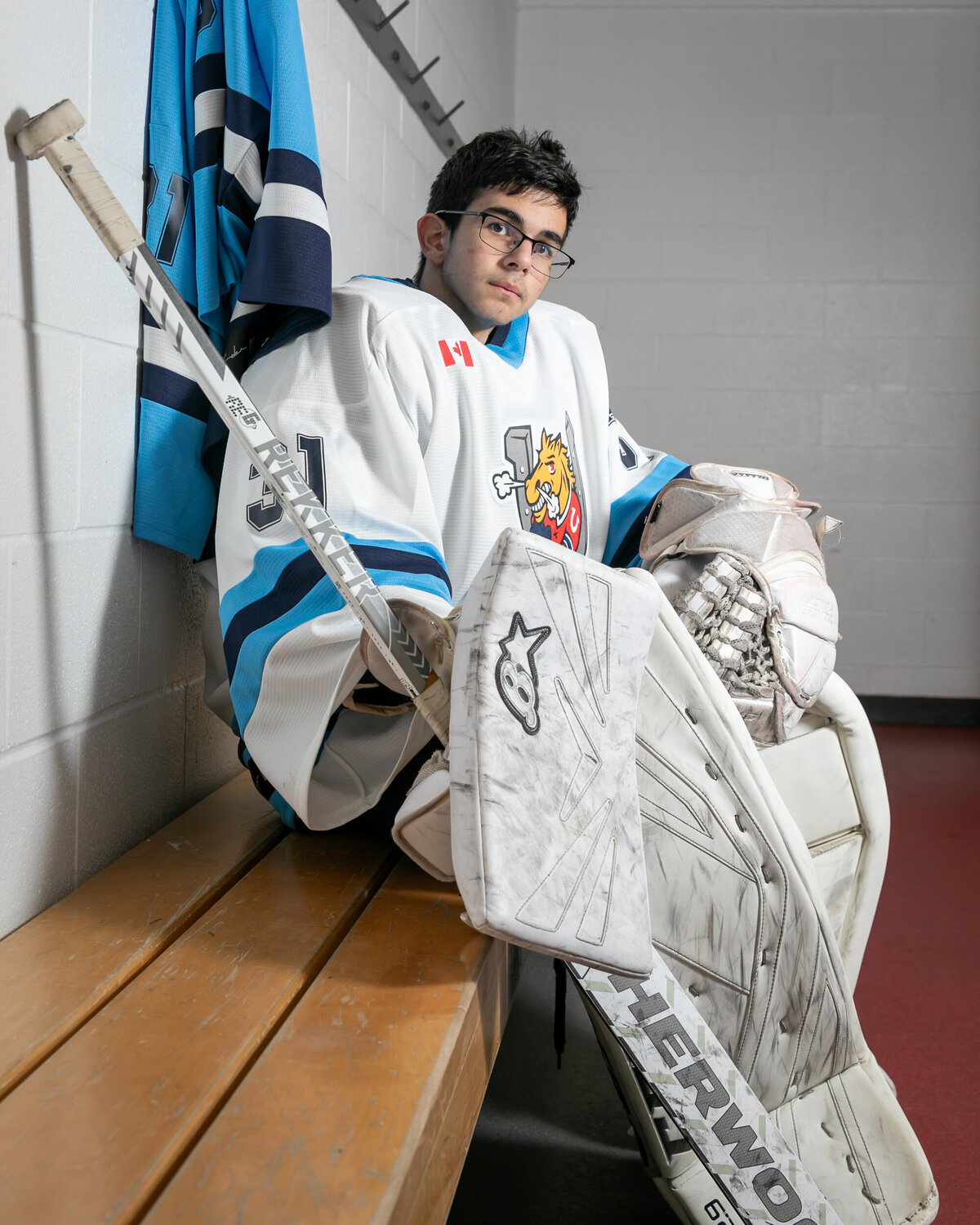 Picture of a goalie sitting in a locker room on a bench. 