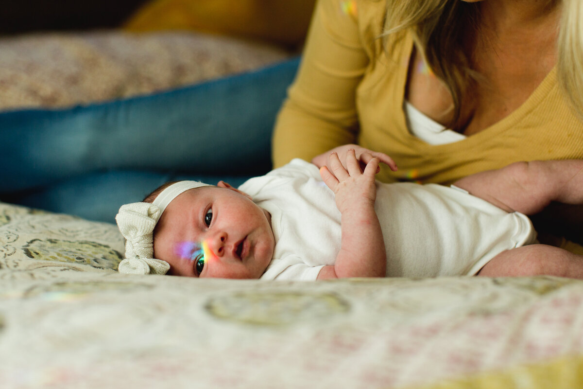 a baby lies on a bed with a prism creating a rainbow on her eye