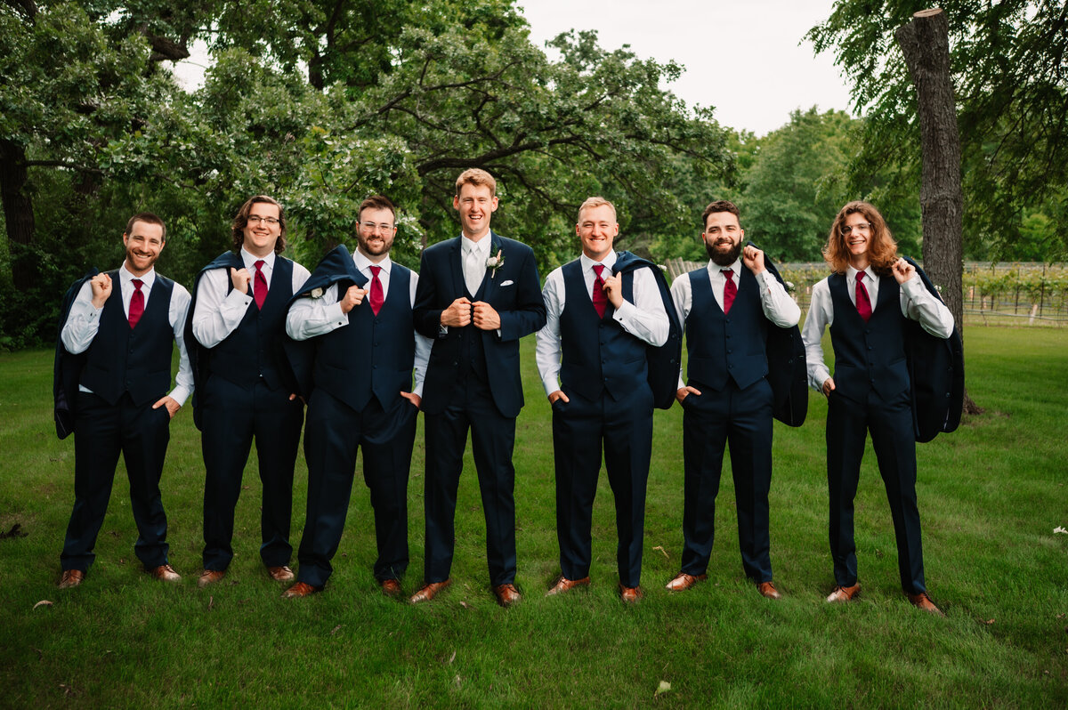 A groom stands with his groomsmen with jackets over their shoulders