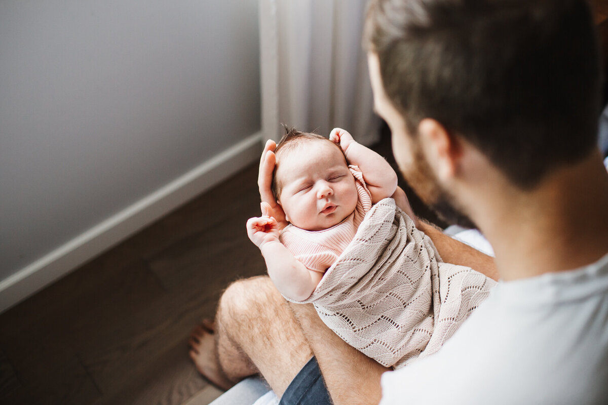 father looking down at swaddled newborn daughter during Mississauga newborn photography session