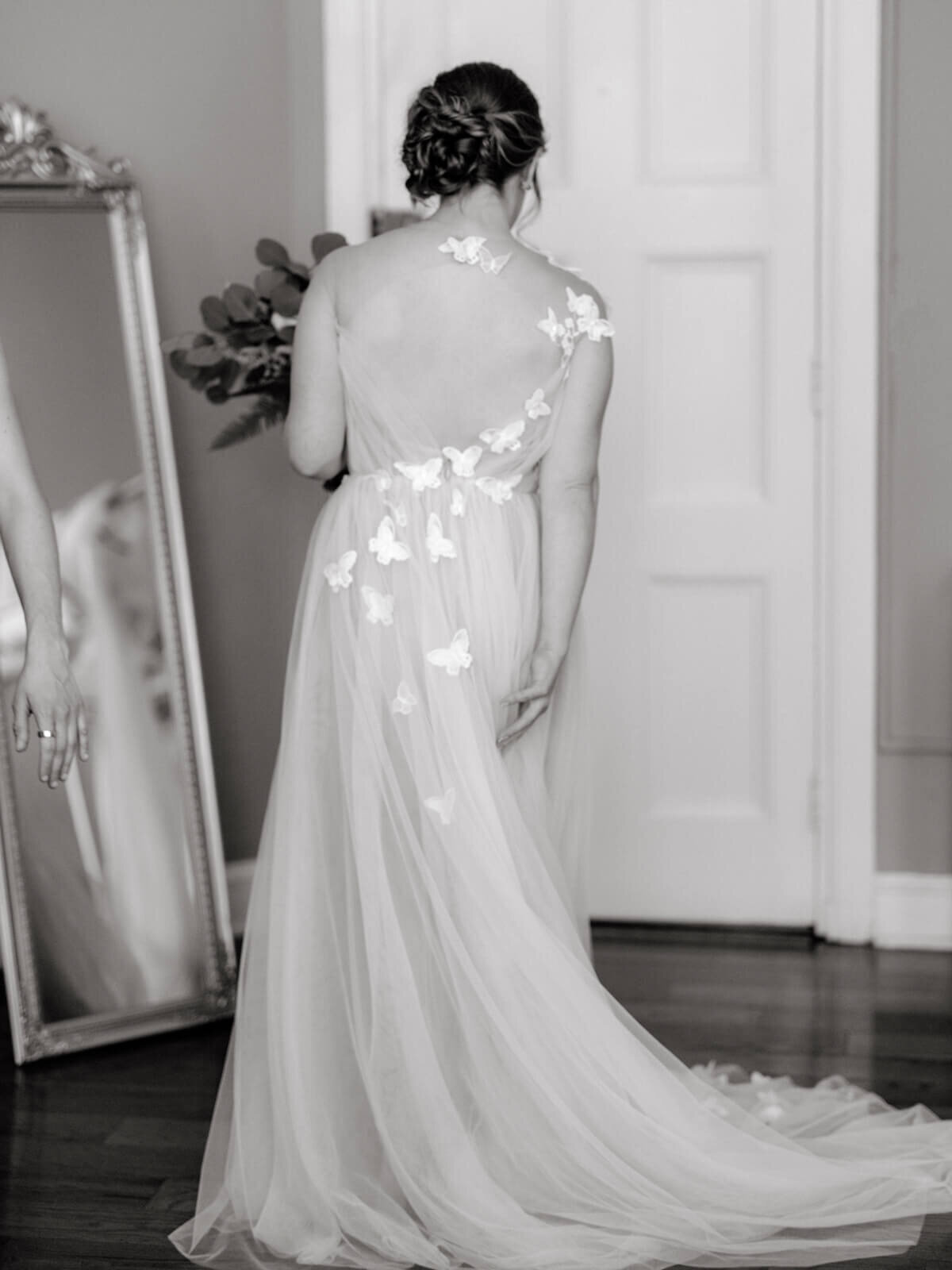 Back view of a bride  facing the door inside a room, with a mirror on the side